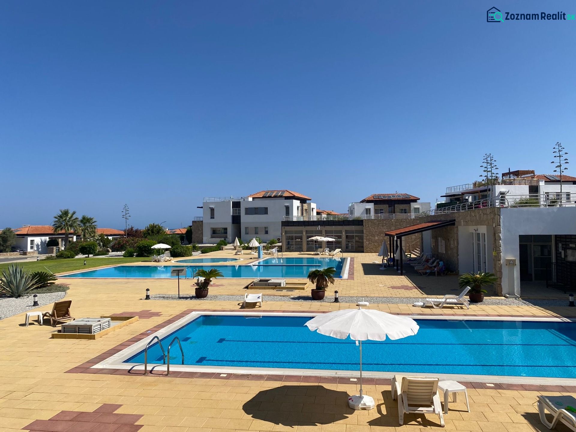 Exterior of the complex in Tatlisu with pools and sunbeds, ideal for a 2-bedroom apartment.
