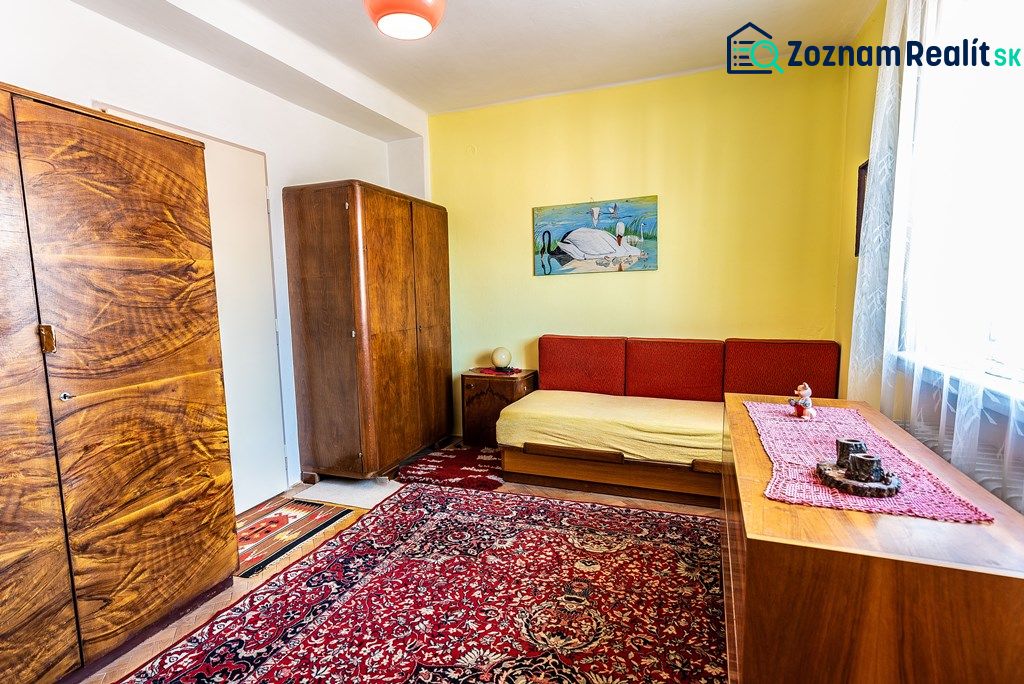 A room in a two-room apartment with wooden furniture and a red carpet.