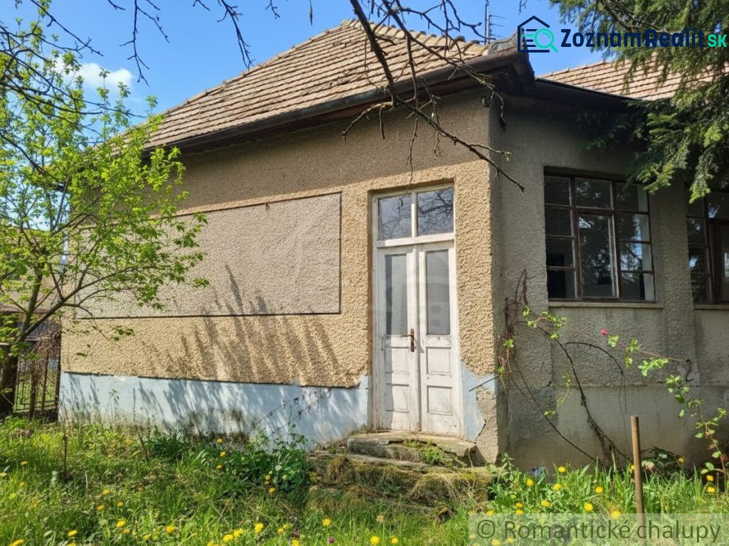 A cottage in Divín with a plastered facade, old windows and doors amidst greenery.