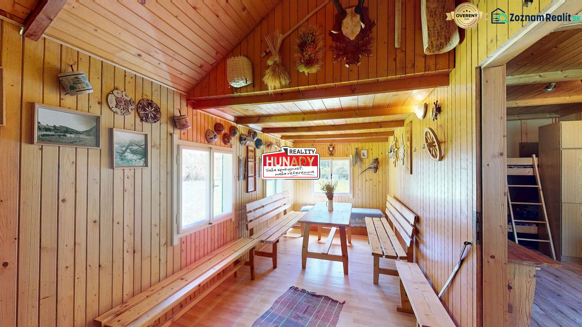 A wooden interior of a cottage with benches and a table, decorations and paintings on the walls.