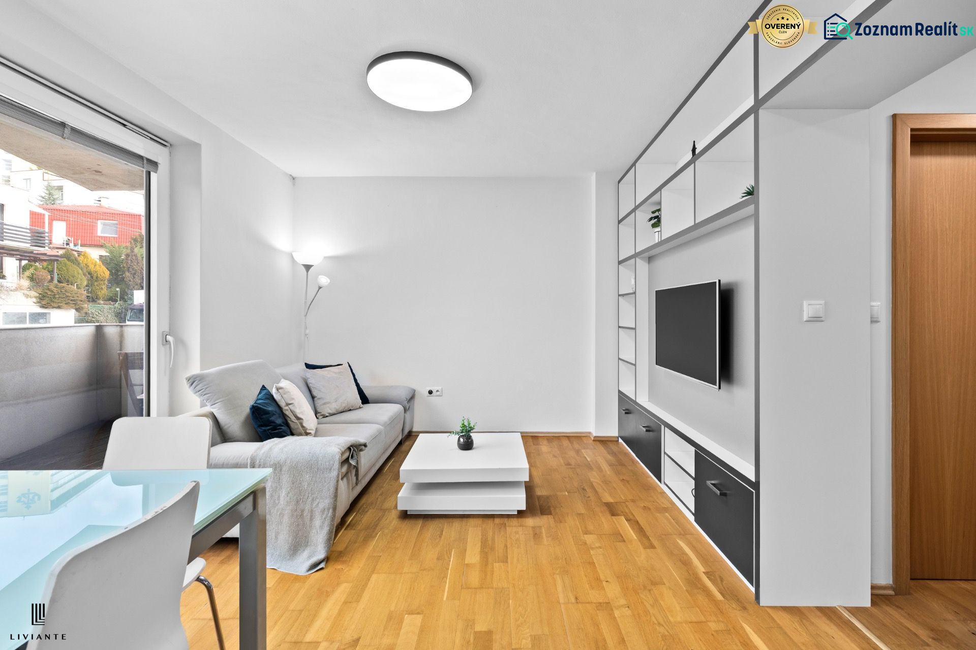 Living room in a two-room apartment with a sofa, TV wall, and wooden decor flooring.