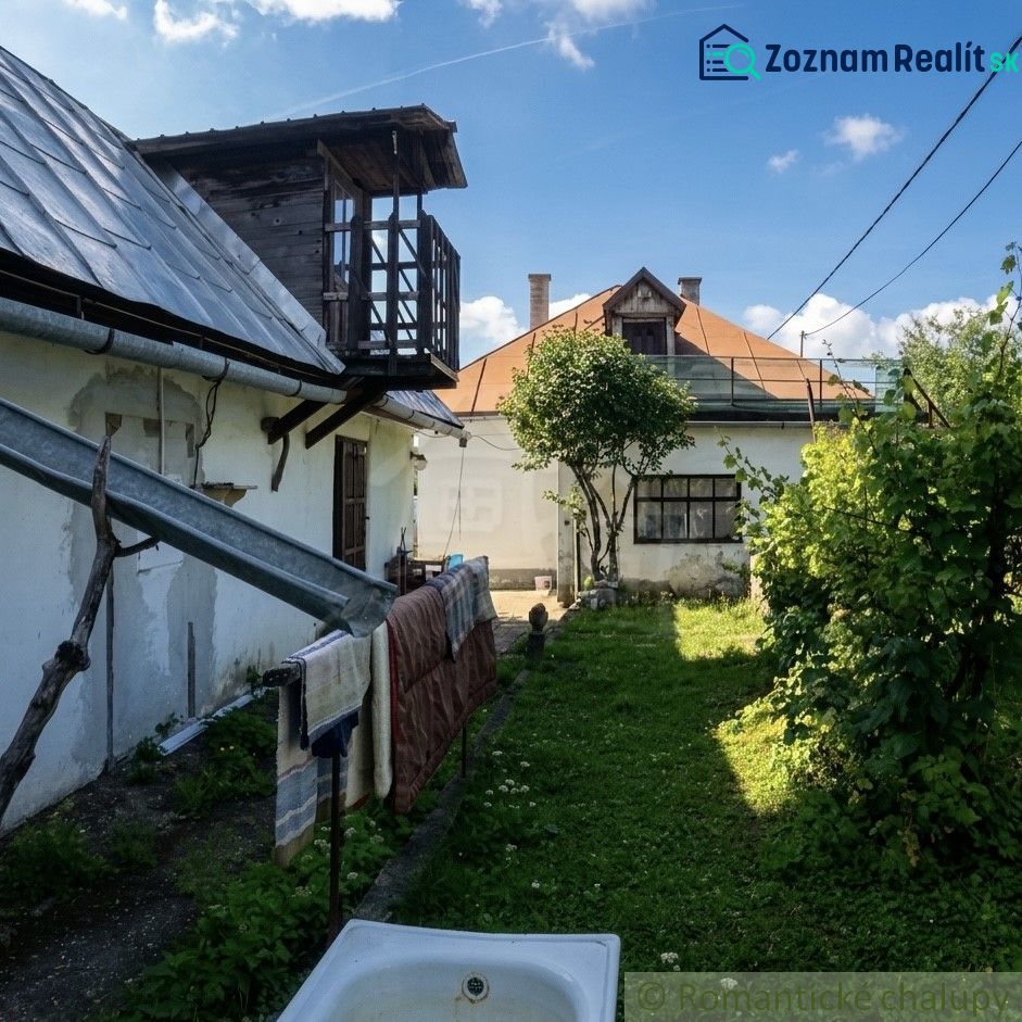 A garden with two buildings of a family house in Štiavnické Bane and a tree in the middle.