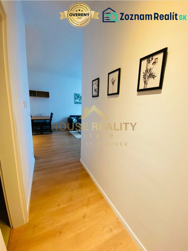 A hallway with a wooden decor floor, pictures on the wall, entrance to the living room in a two-room apartment.