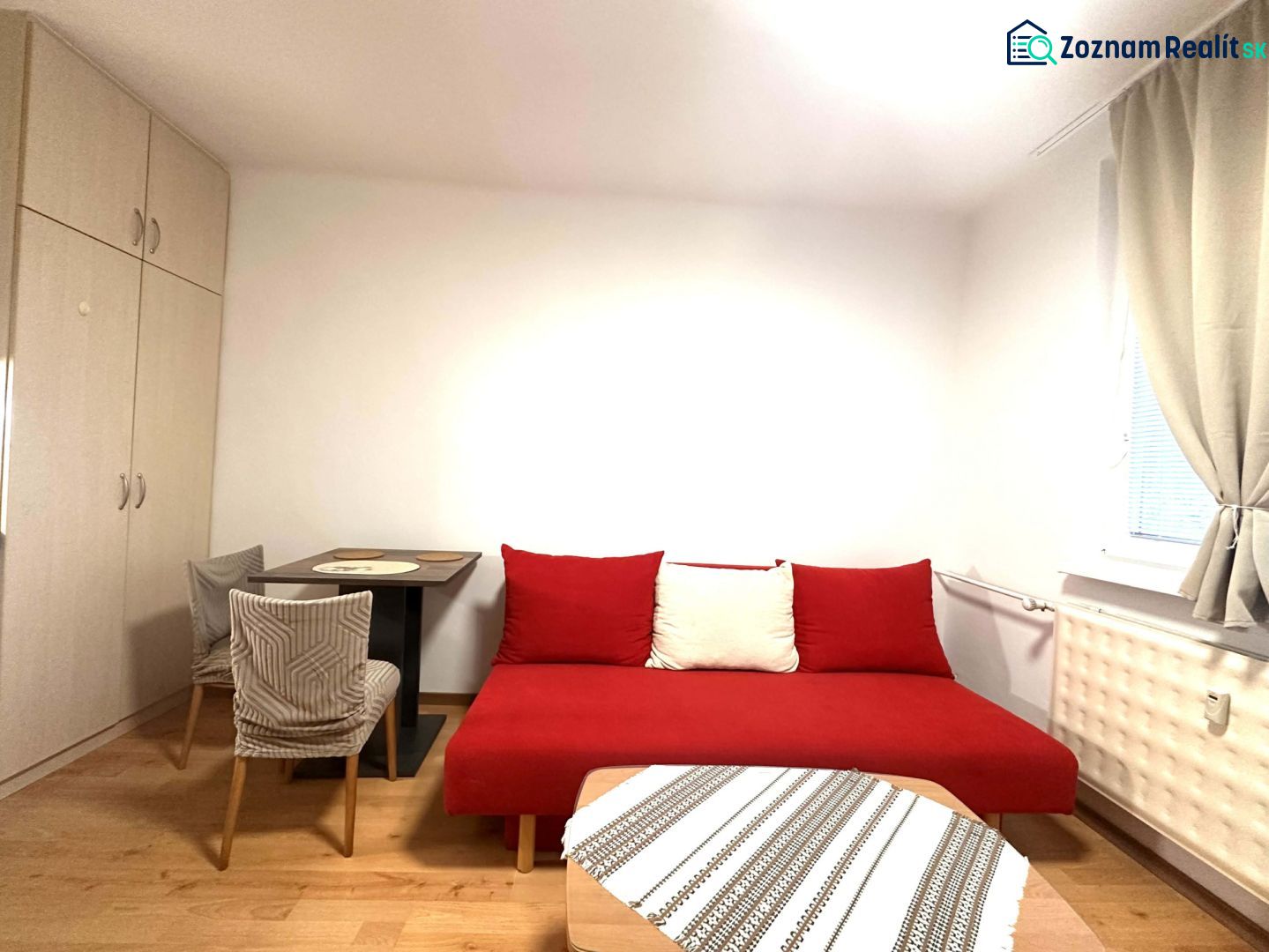 A room in a recreational apartment with a red sofa, a table, and a wooden-patterned floor.