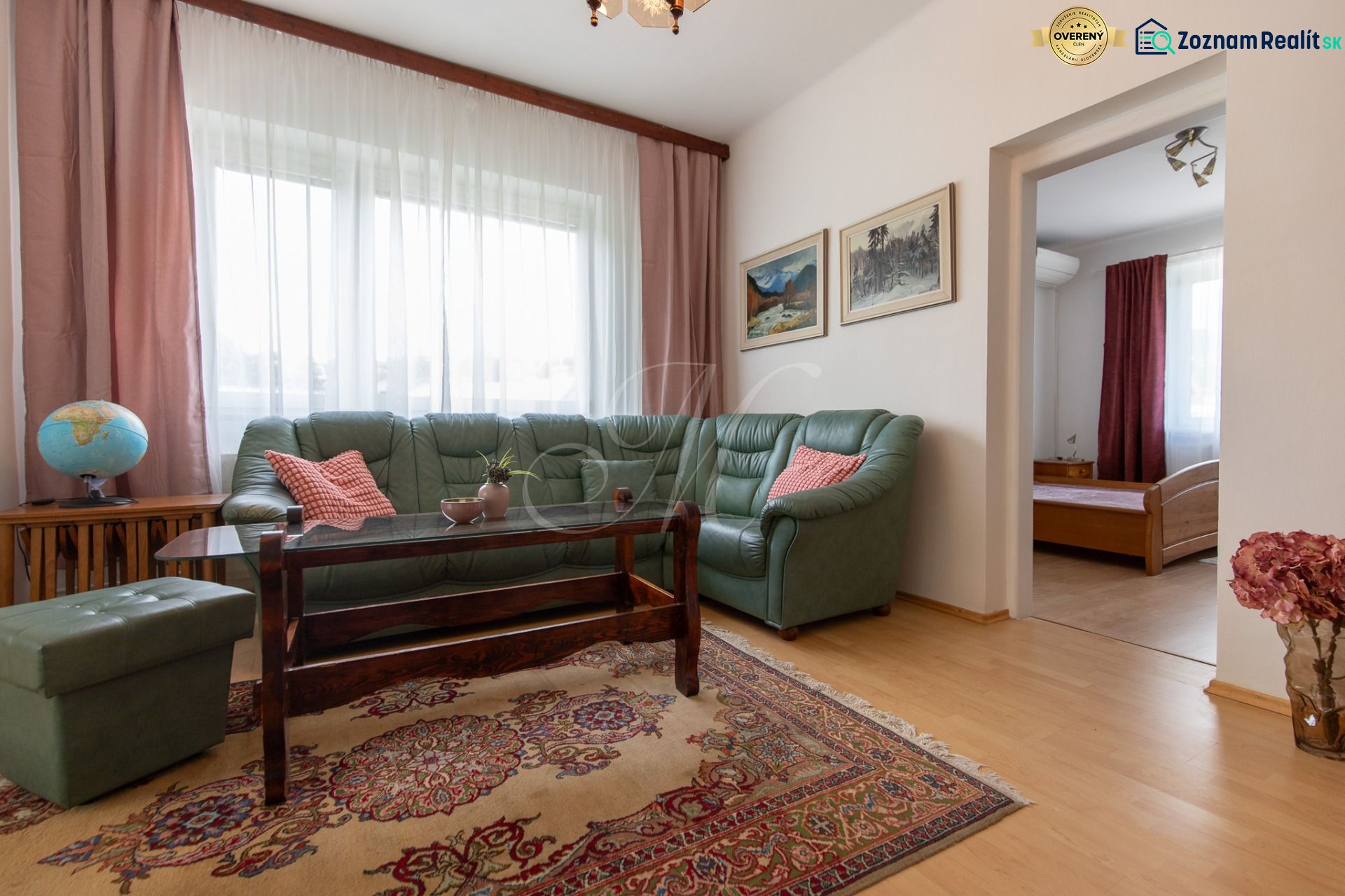 A living room with a wood-patterned floor, a green sofa, and an oriental rug in a three-room apartment.