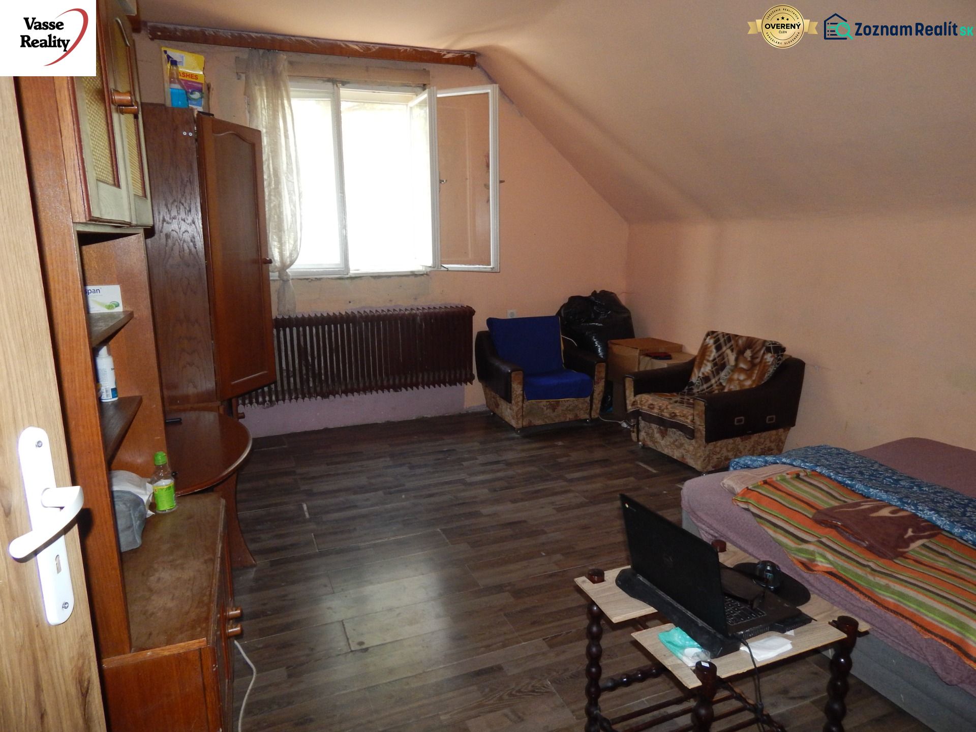 A room in a family house with a wooden decor floor, simple furnishings, and an open window.
