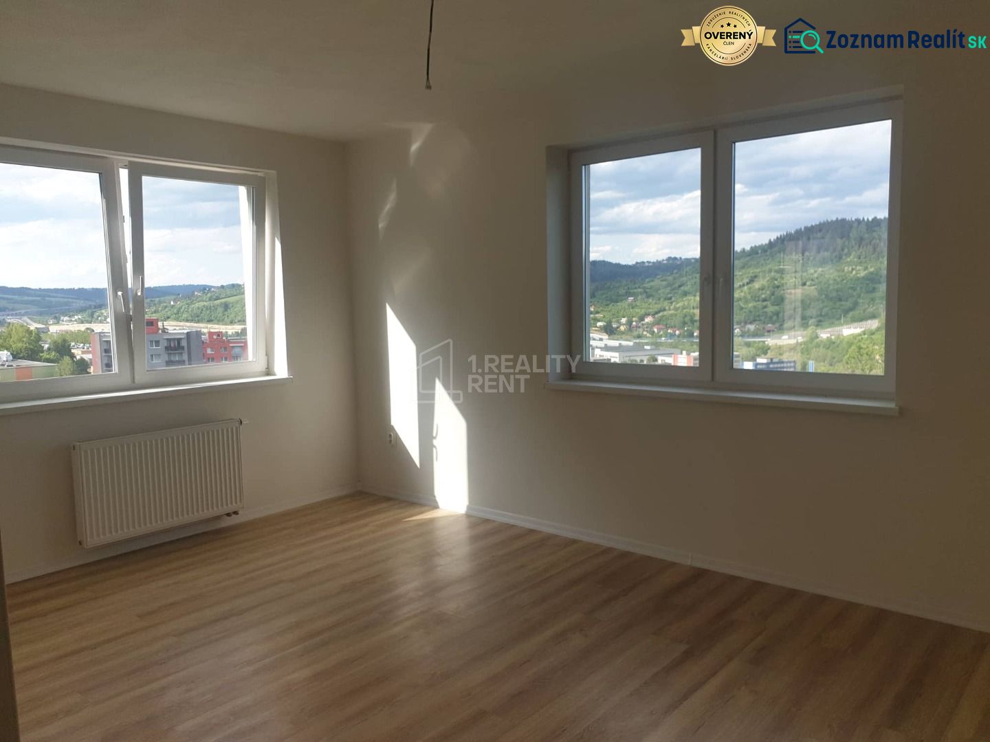 A bright empty room with wood-patterned flooring and large windows in a studio apartment.