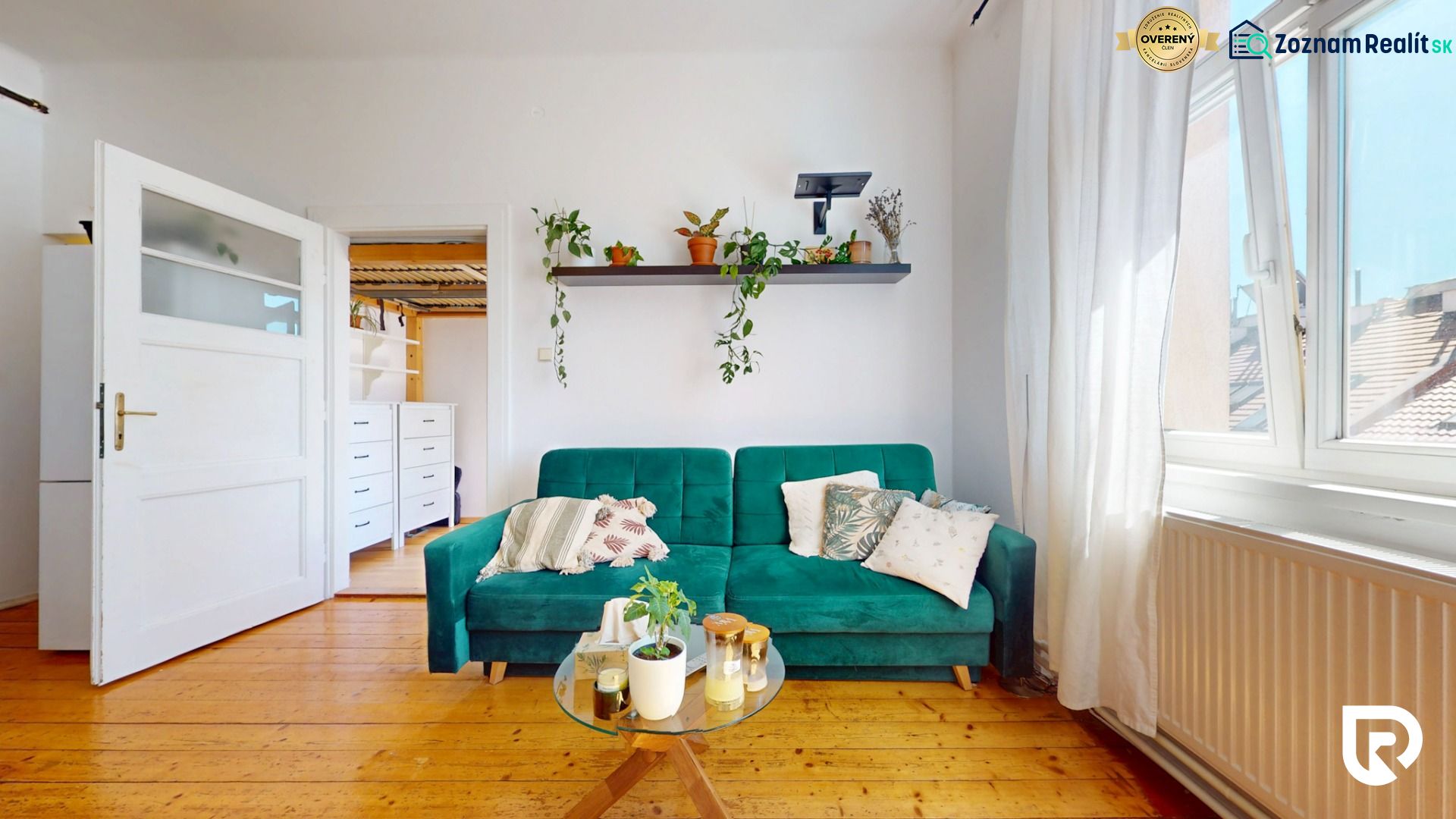 Living room with a green sofa, a shelf with plants, and a wooden decor floor.
