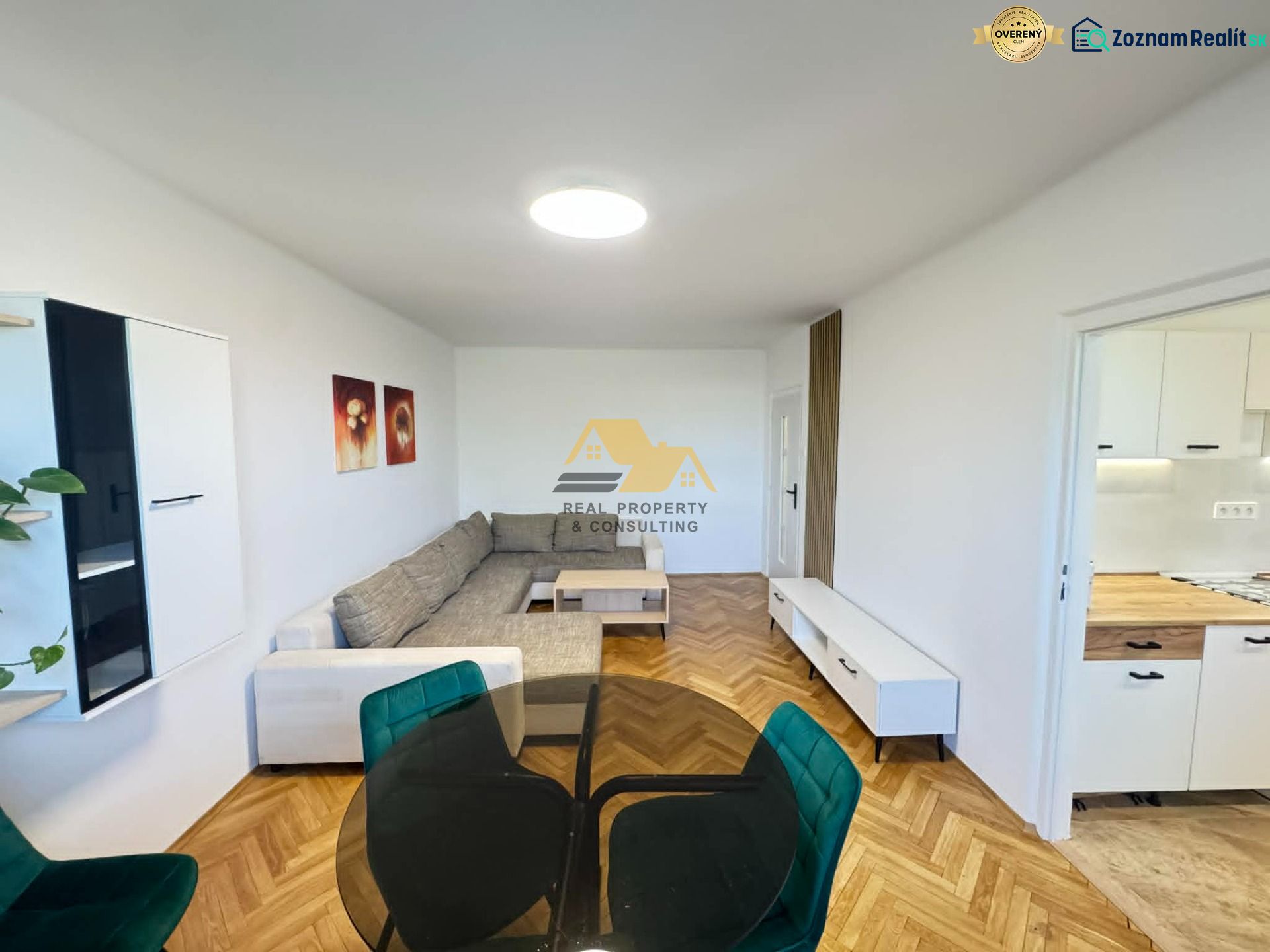 Bright living room with a sofa, wood-patterned flooring, and a kitchen in a 2-room apartment.