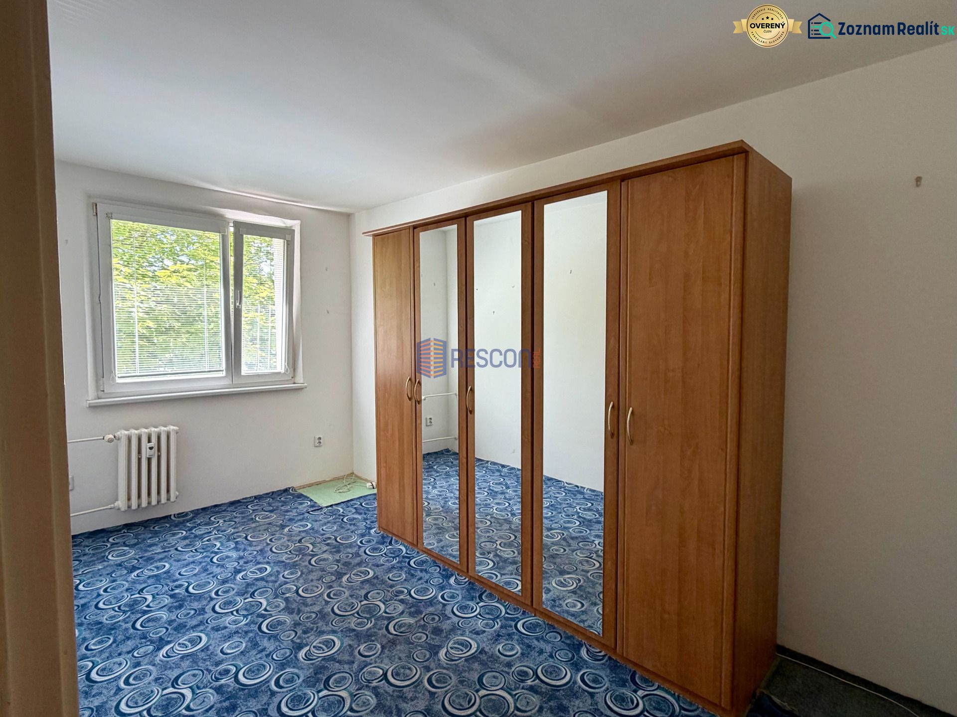 A room with a wardrobe and a window, blue carpet, 4-room apartment.