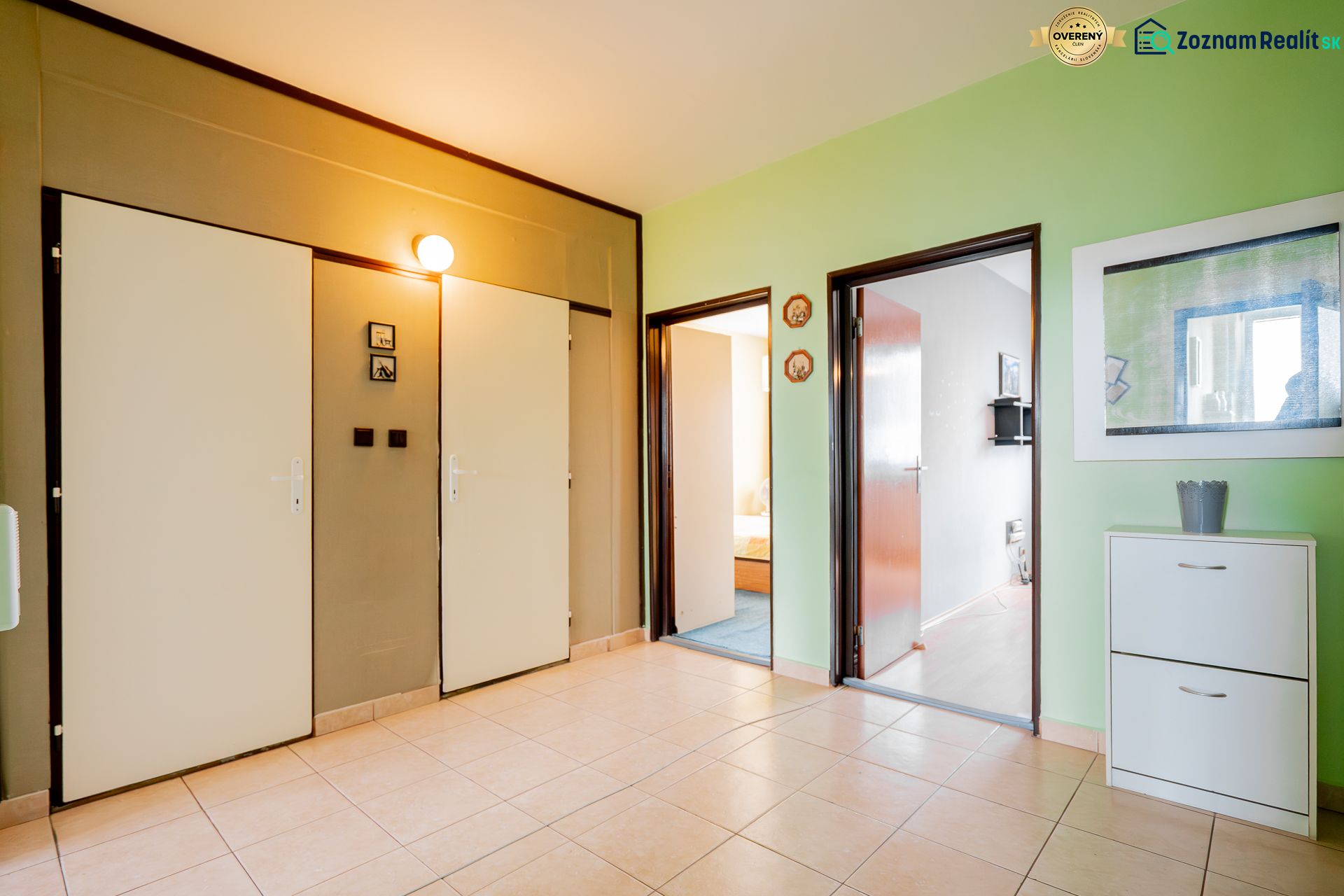 A hallway in a 3-room apartment with a ceramic floor, green wall, and bright lighting.