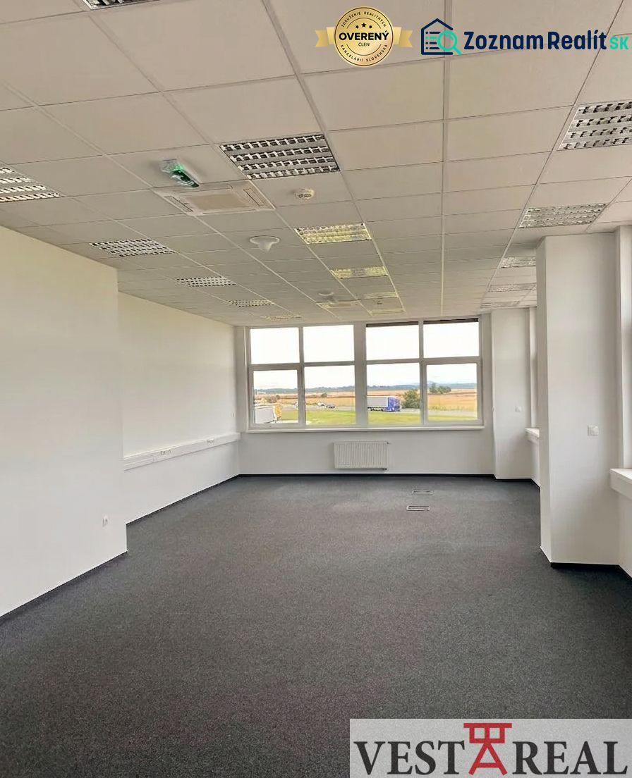 Office spaces with carpet flooring and a large window in a warehouse and hall building.