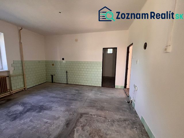 A room in a family house with an unfinished floor and green tiles.