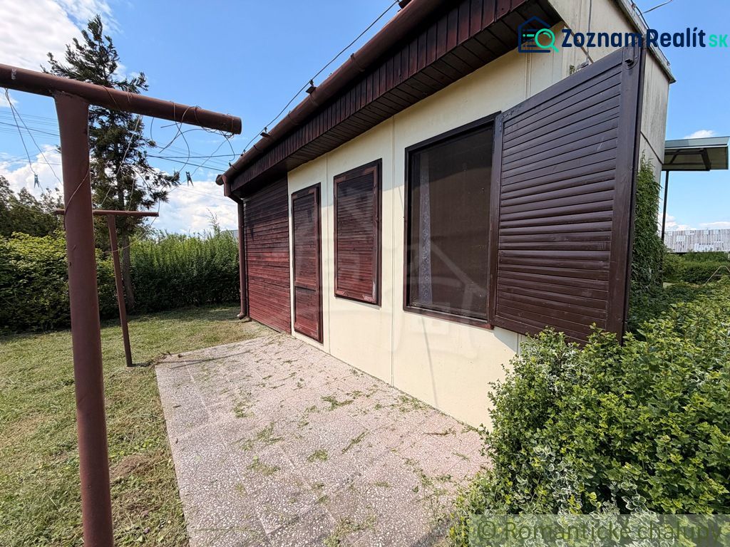 A cottage in Nové Zámky with closed wooden shutters and surrounding greenery in the garden.
