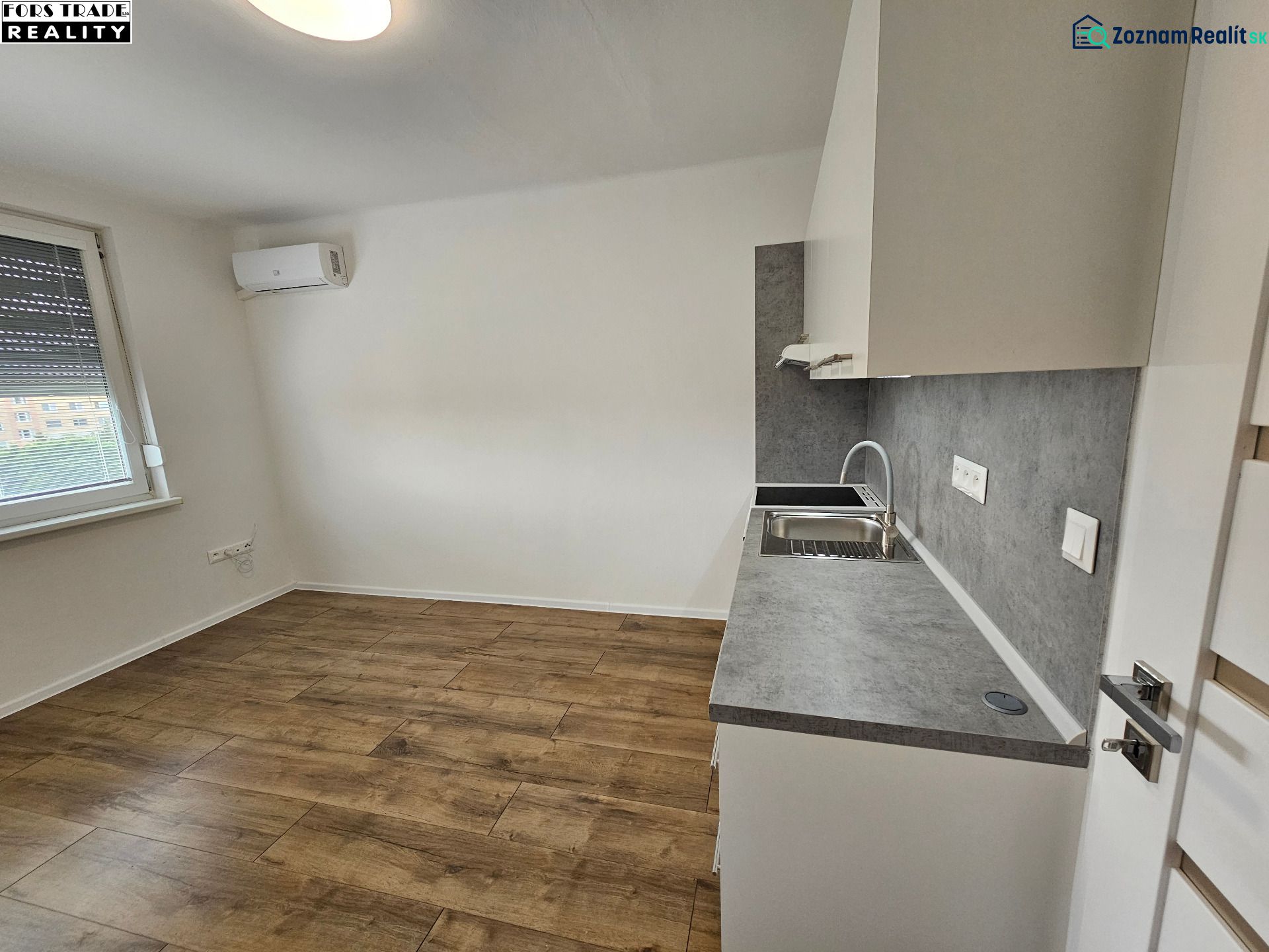 Studio apartment with a kitchenette and wooden decor flooring, air conditioning, and a window.