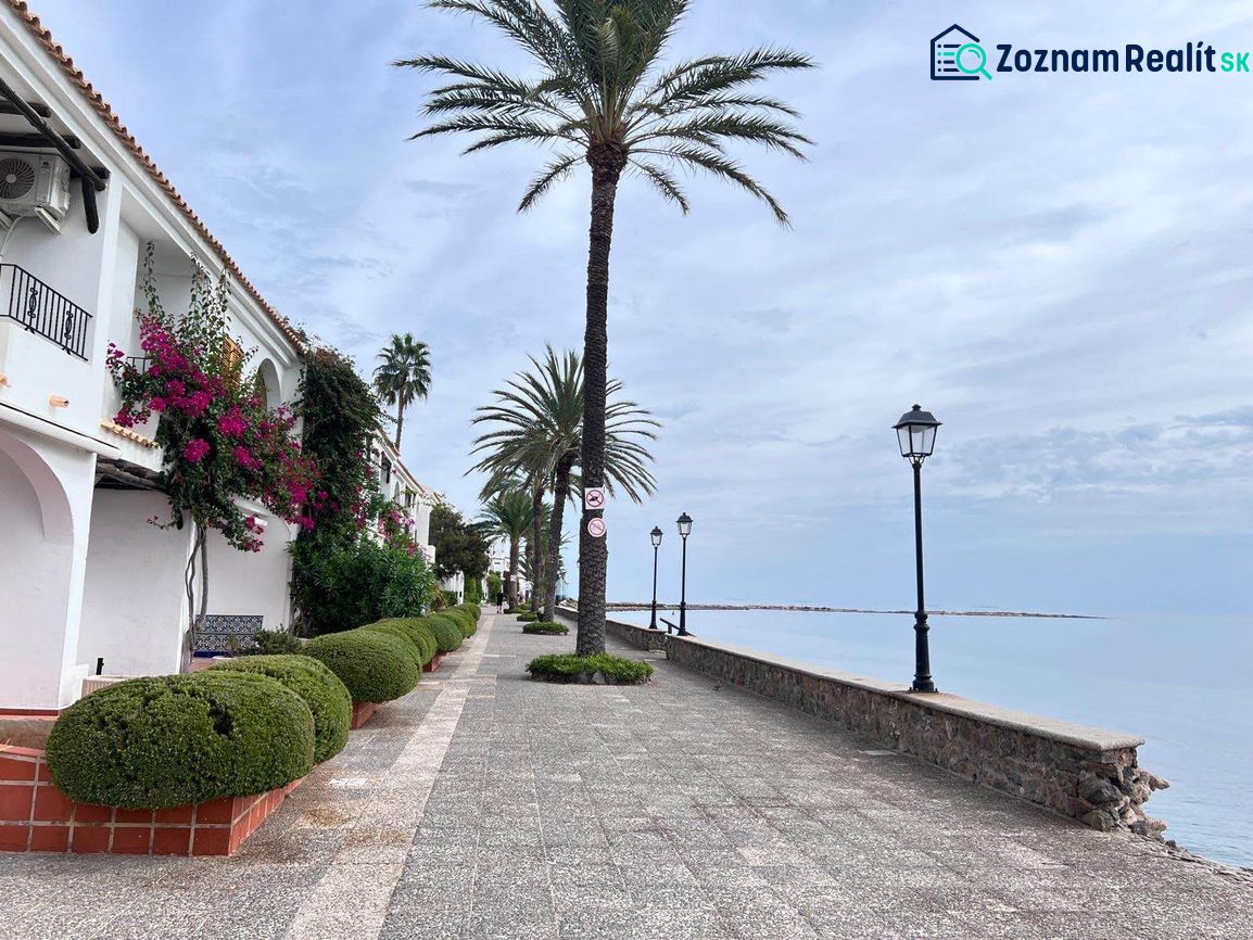 Seaside promenade in La Manga del Mar Menor, Spain, lined with palm trees and lamps.