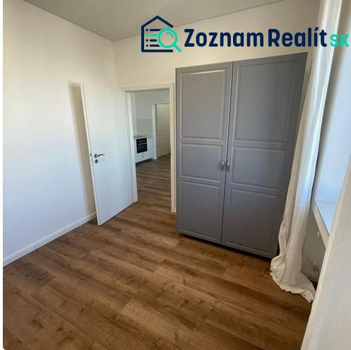 A room in a 3-room apartment with a wooden decor floor, a gray wardrobe, and a window.