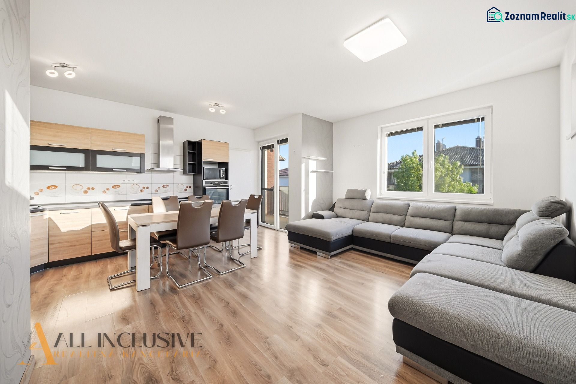 Living room with kitchen, large gray sofa, wooden decor flooring, 3-room apartment.