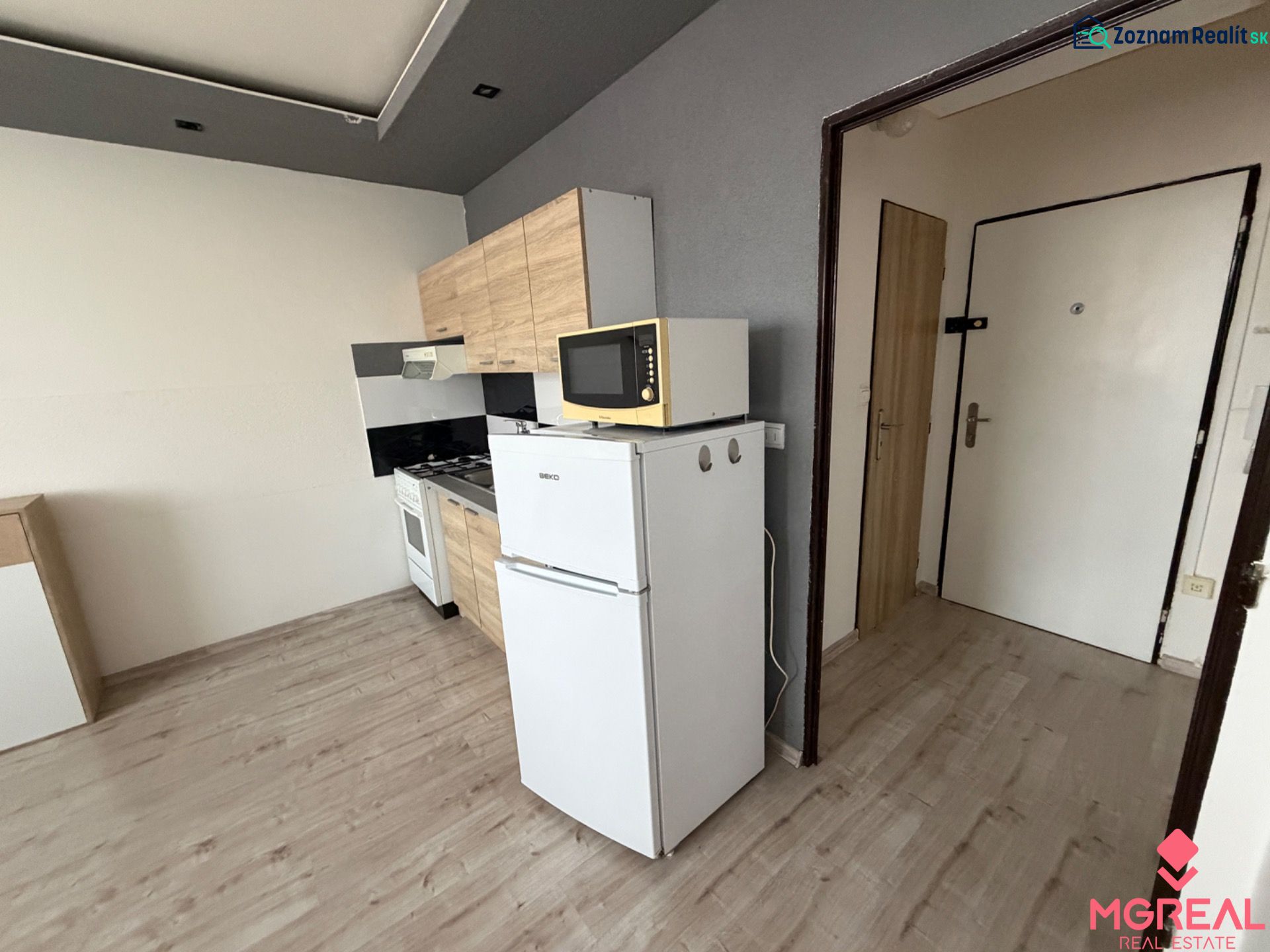 Kitchen in a studio apartment with a refrigerator and a wooden decor floor.