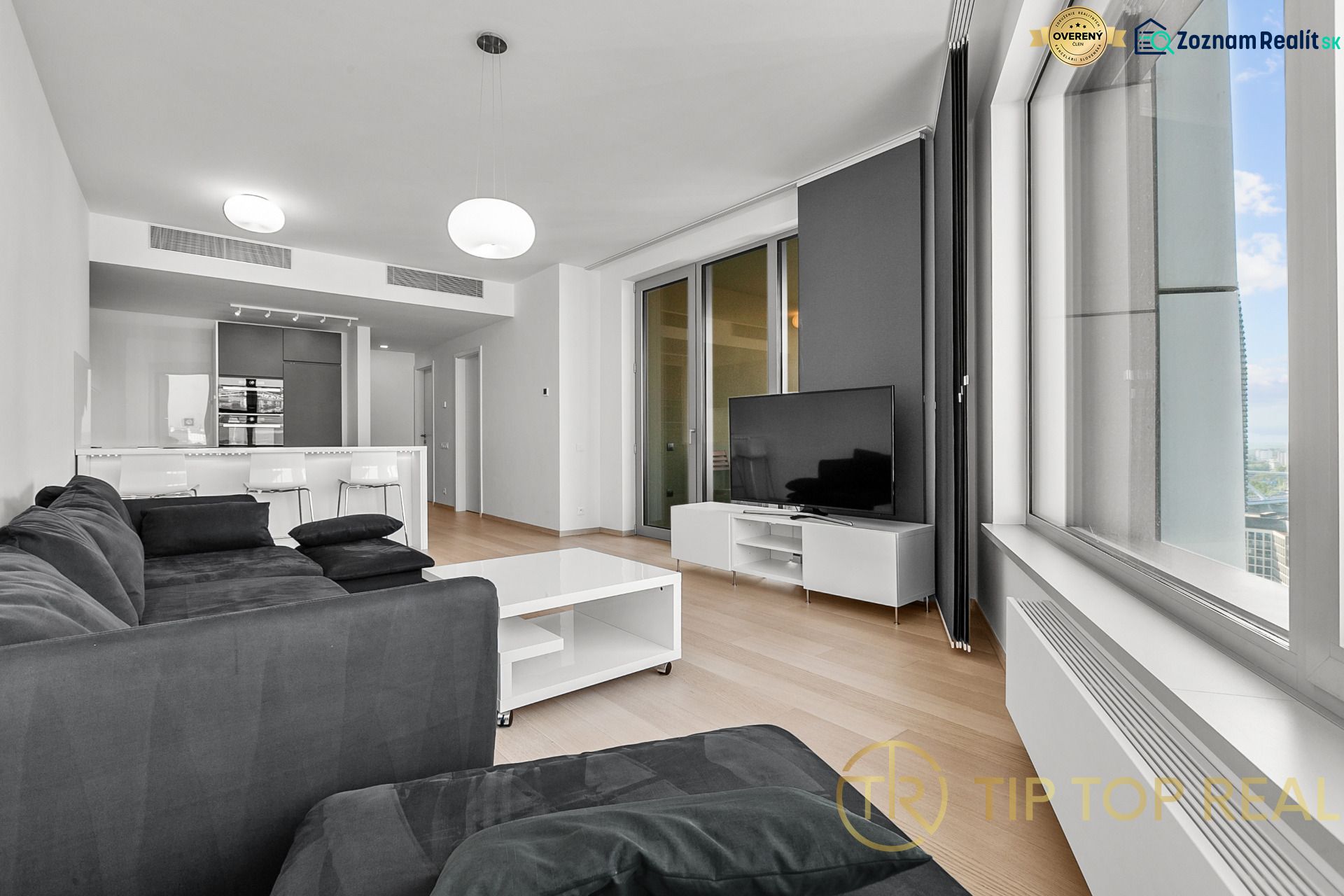 Living room with a dark sofa and a television, on Továrenská street, part of a 3-room apartment.