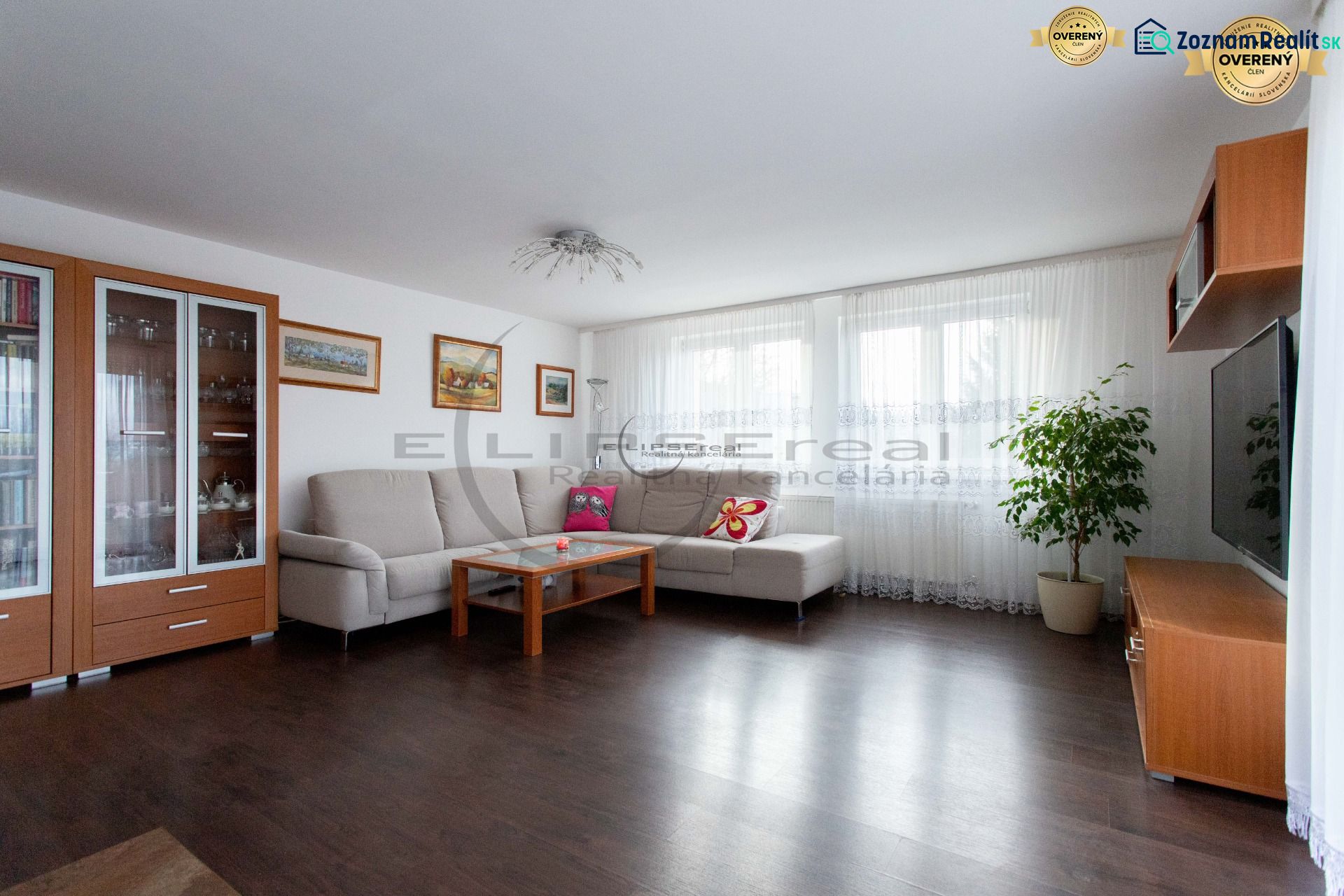 Living room in a family house with a sofa, television, and wooden-patterned flooring.