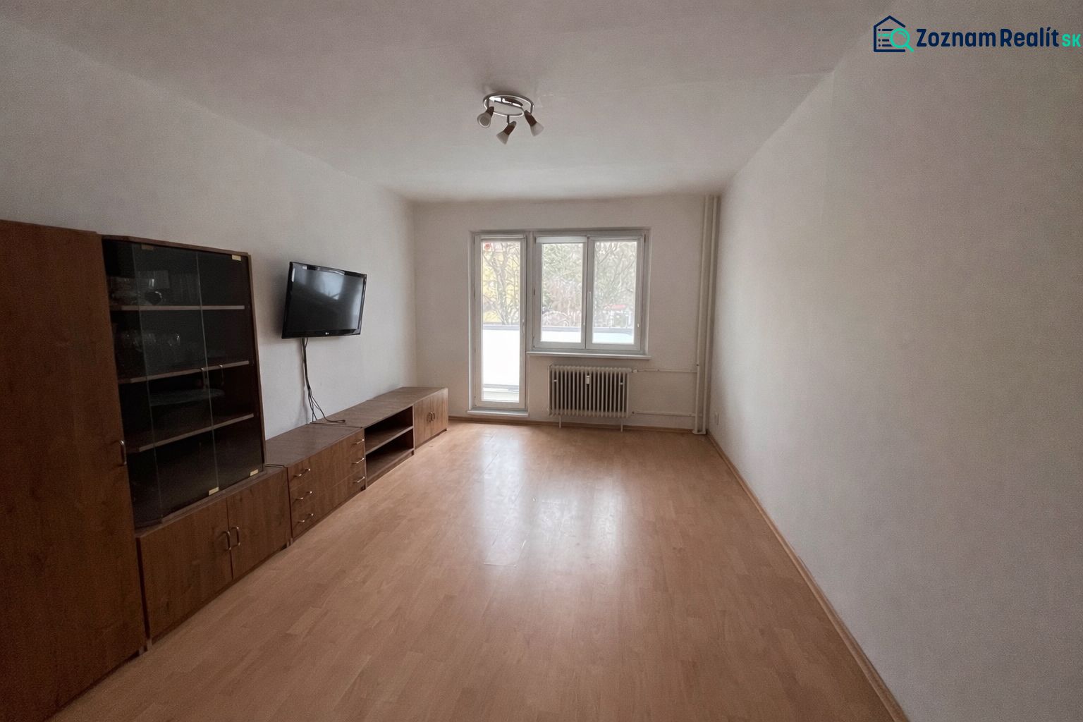 Living room in a two-room apartment with a wooden decor floor and a television on the wall.