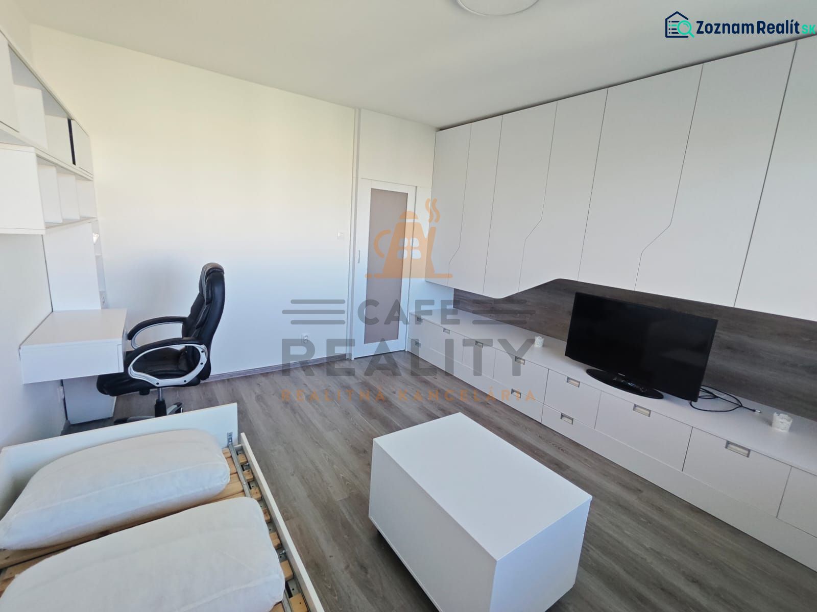 Interior of a 1-bedroom apartment with a desk, television, and wood-patterned flooring.