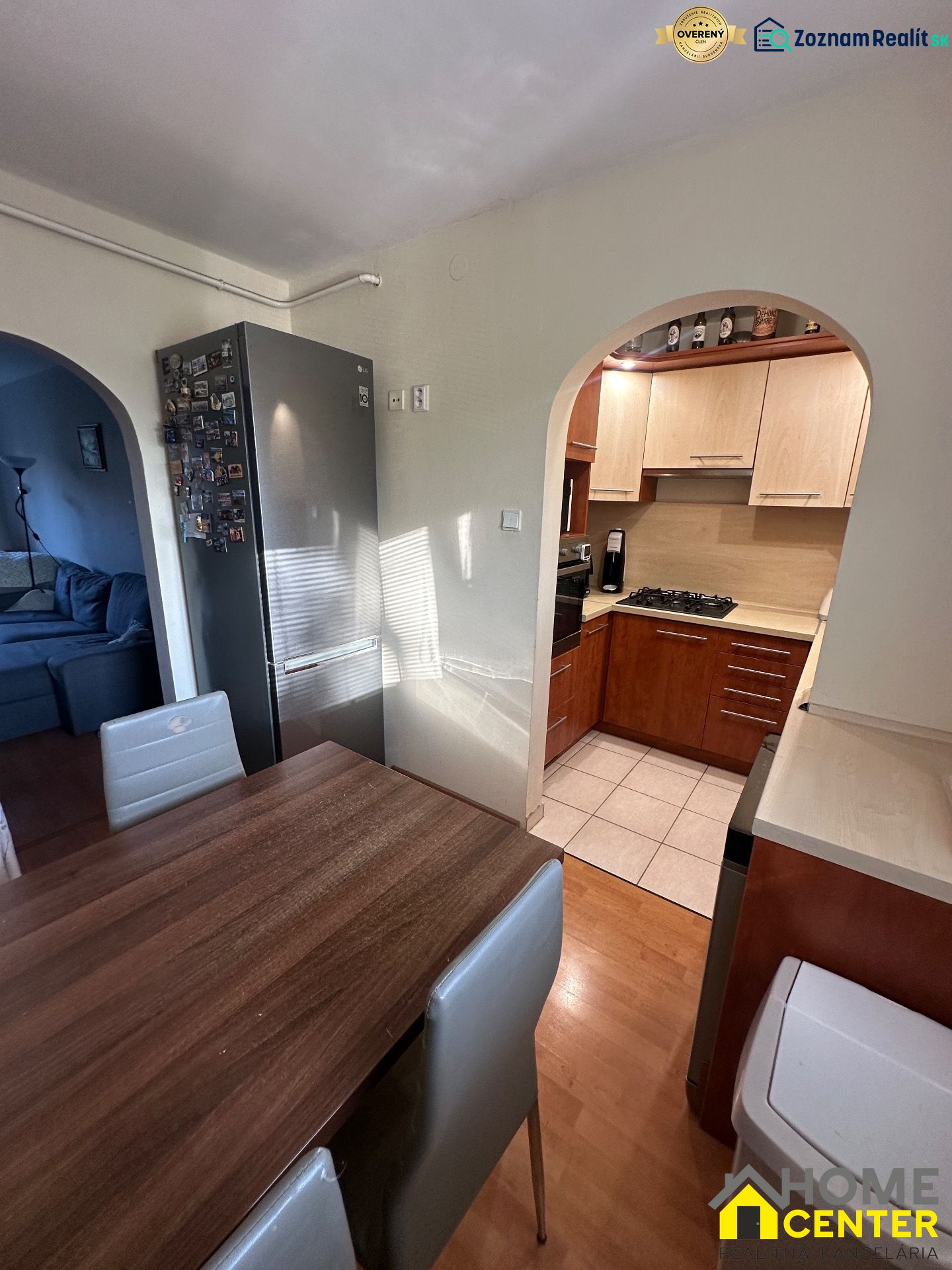 A kitchen with wooden decor, a dining table, a refrigerator, and an arch leading to the living room.