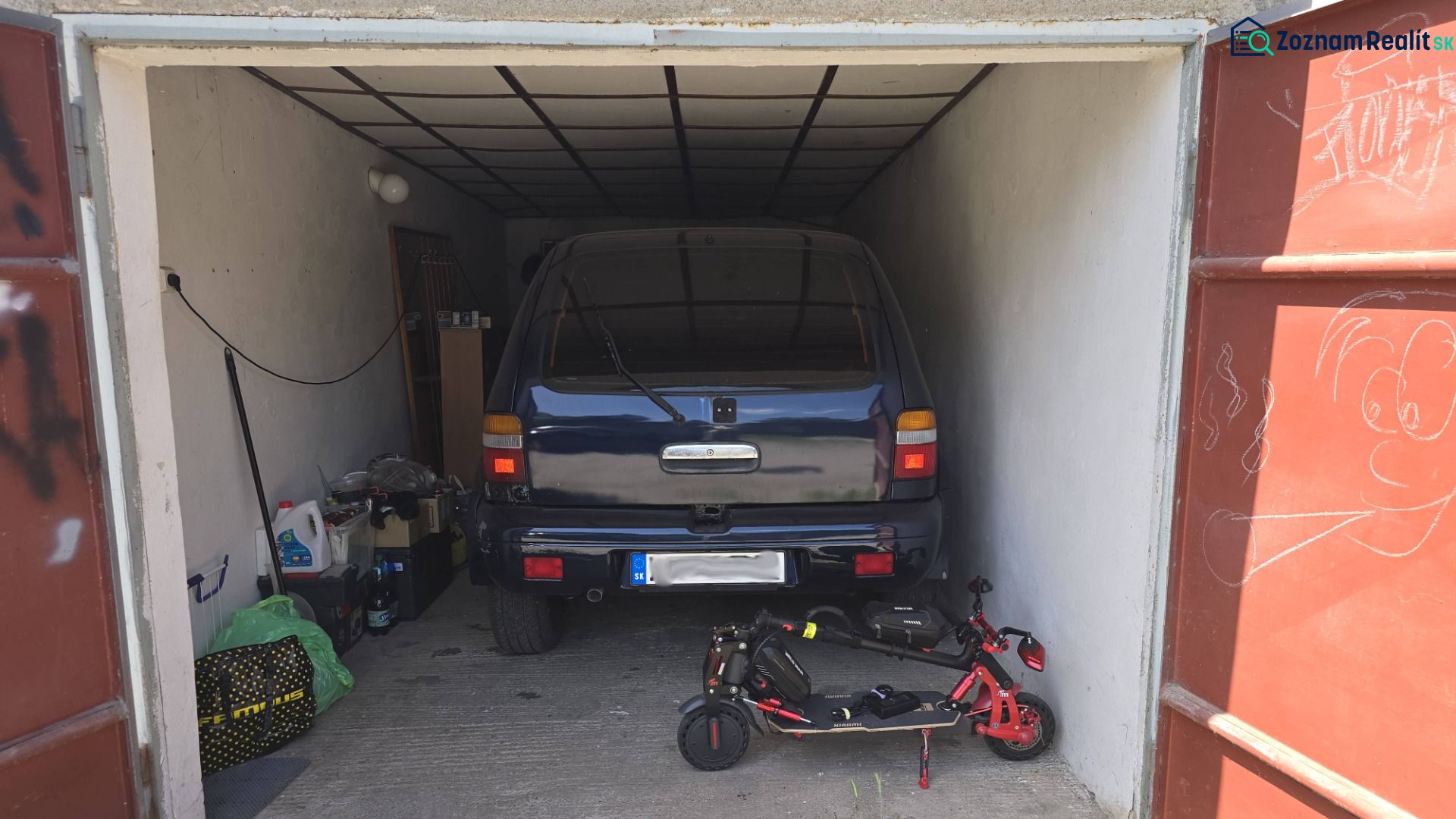 A garage with a car and an electric scooter, stored items, and a drawing on the door.