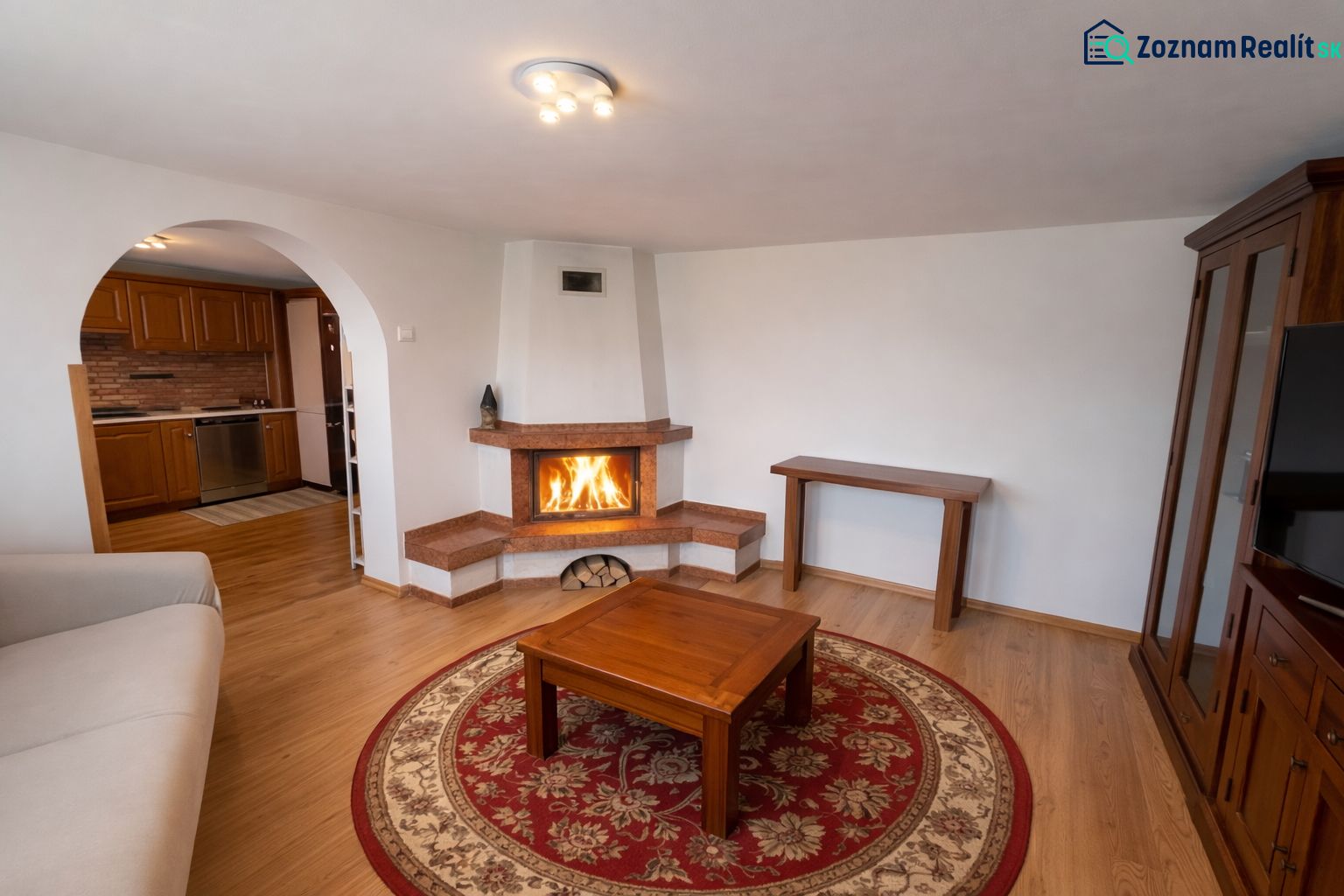 Living room in a family house with a fireplace, wooden decor flooring, and an arched doorway.