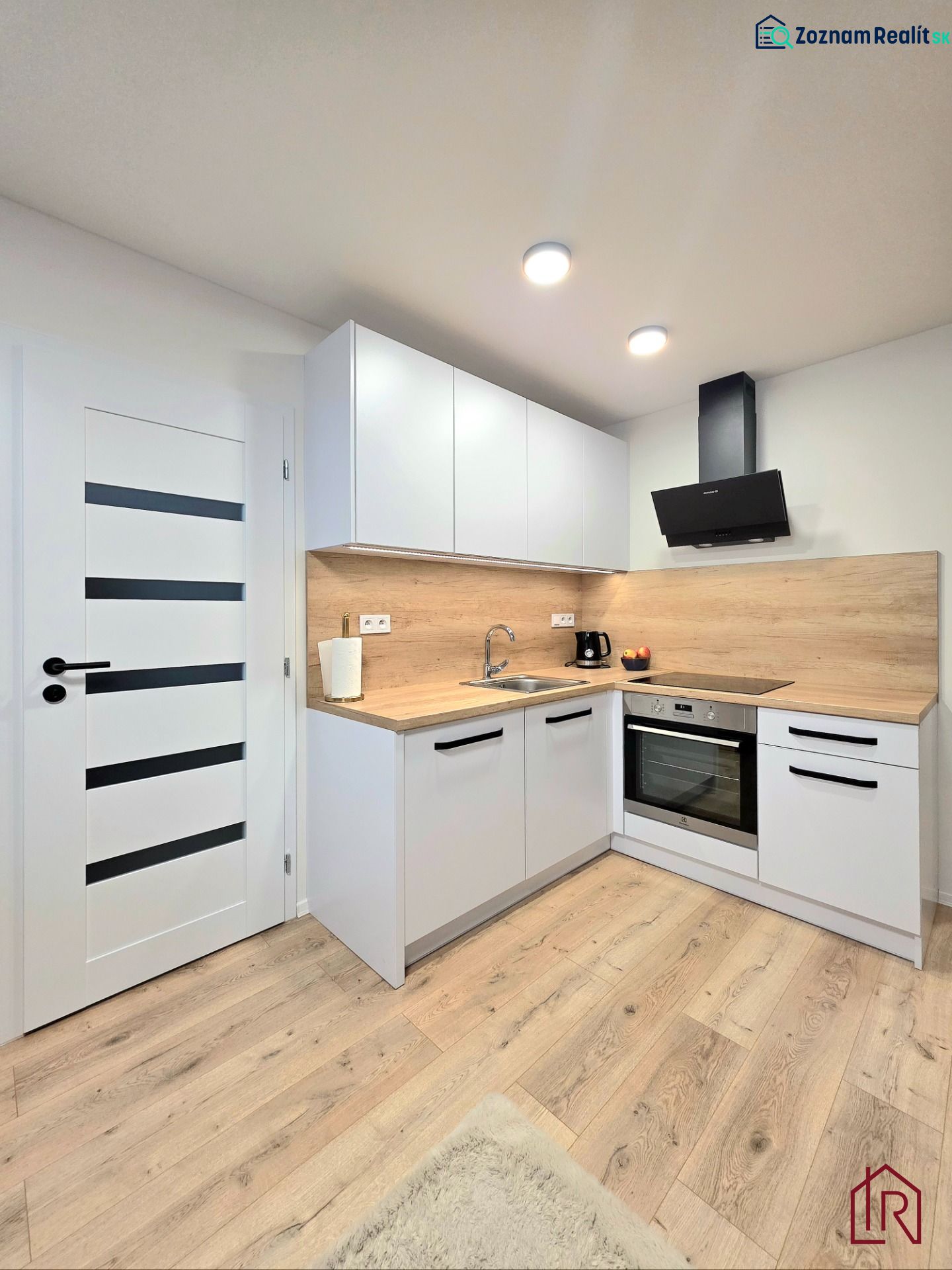 A kitchen in a 2-room apartment with white cabinets and a wood-patterned floor.