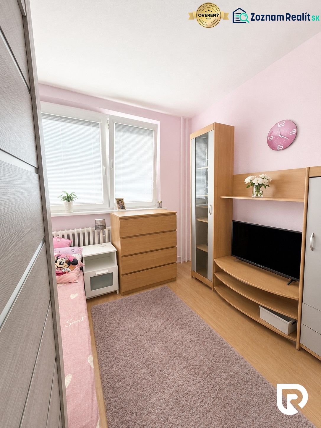 Children's room with wood-patterned flooring, pink walls, and wooden furniture in a three-room apartment.