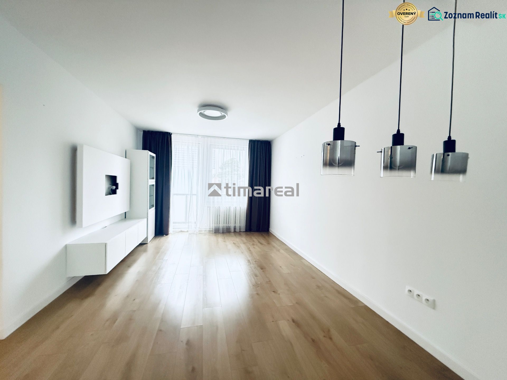 Living room in a three-room apartment with a wooden decor floor and hanging lamps.