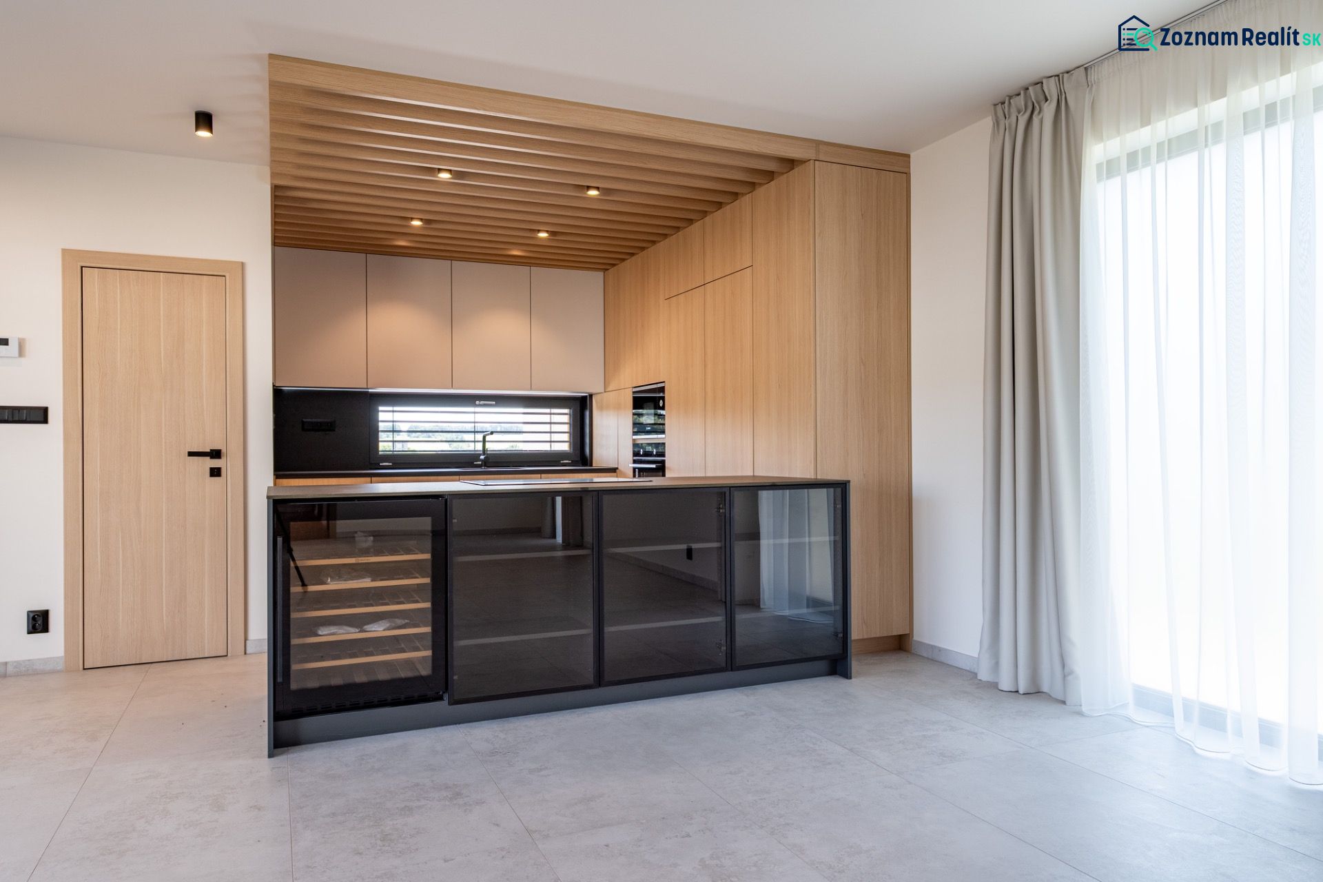 A kitchen with wooden decor, a glass wine cabinet, and a large window in a family house.