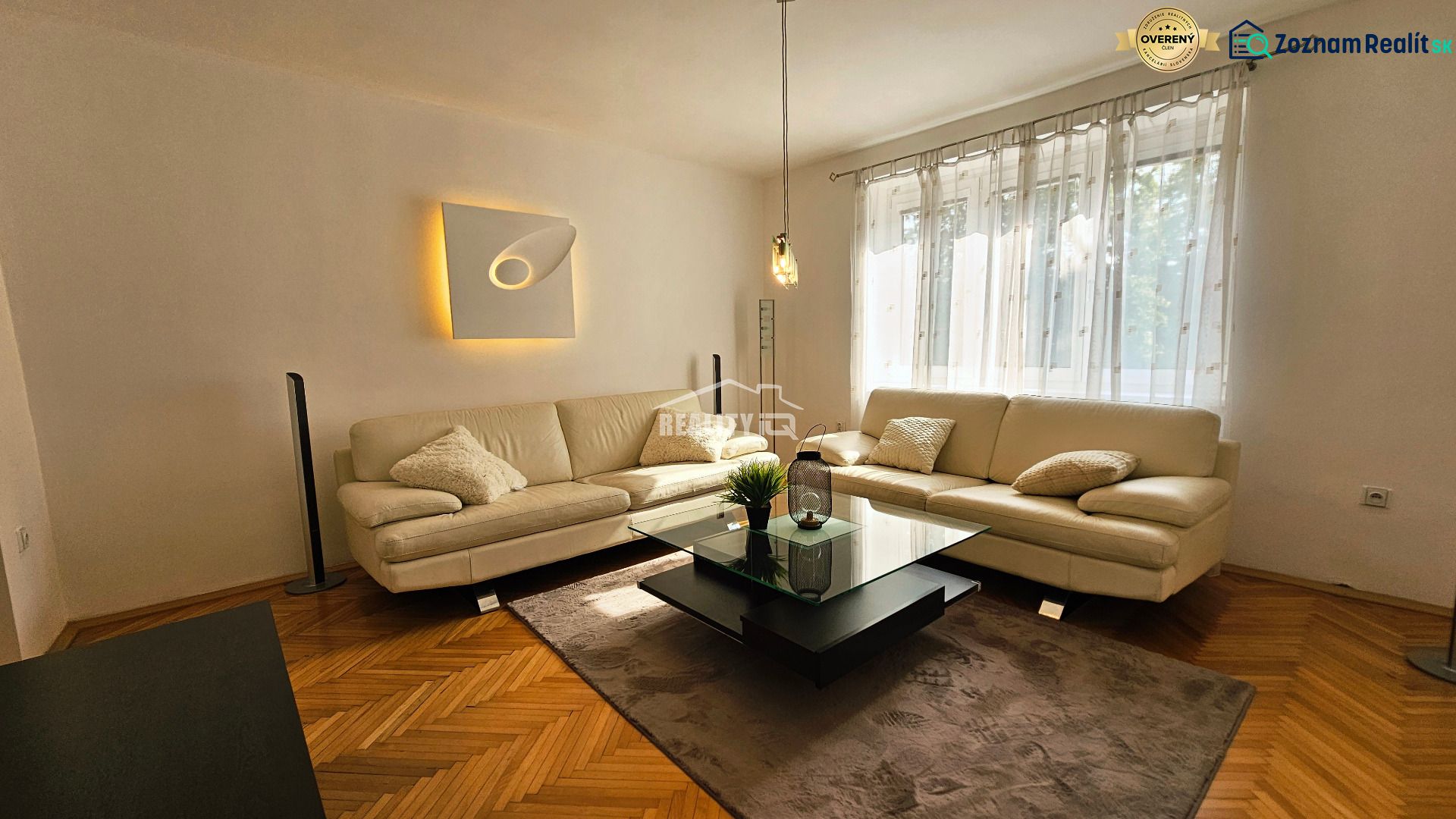 Living room in a 2-room apartment with a white couch and a wooden decor floor.