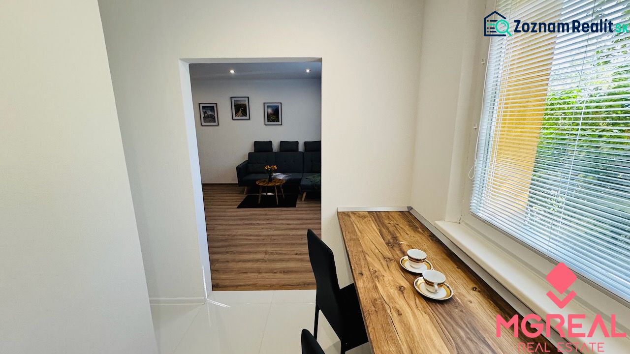 Interior of a 1-room apartment with a wooden decor floor, a sofa, and a table by the window.