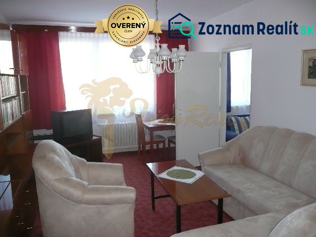 Living room in a two-room apartment with a red carpet and a beige sofa.