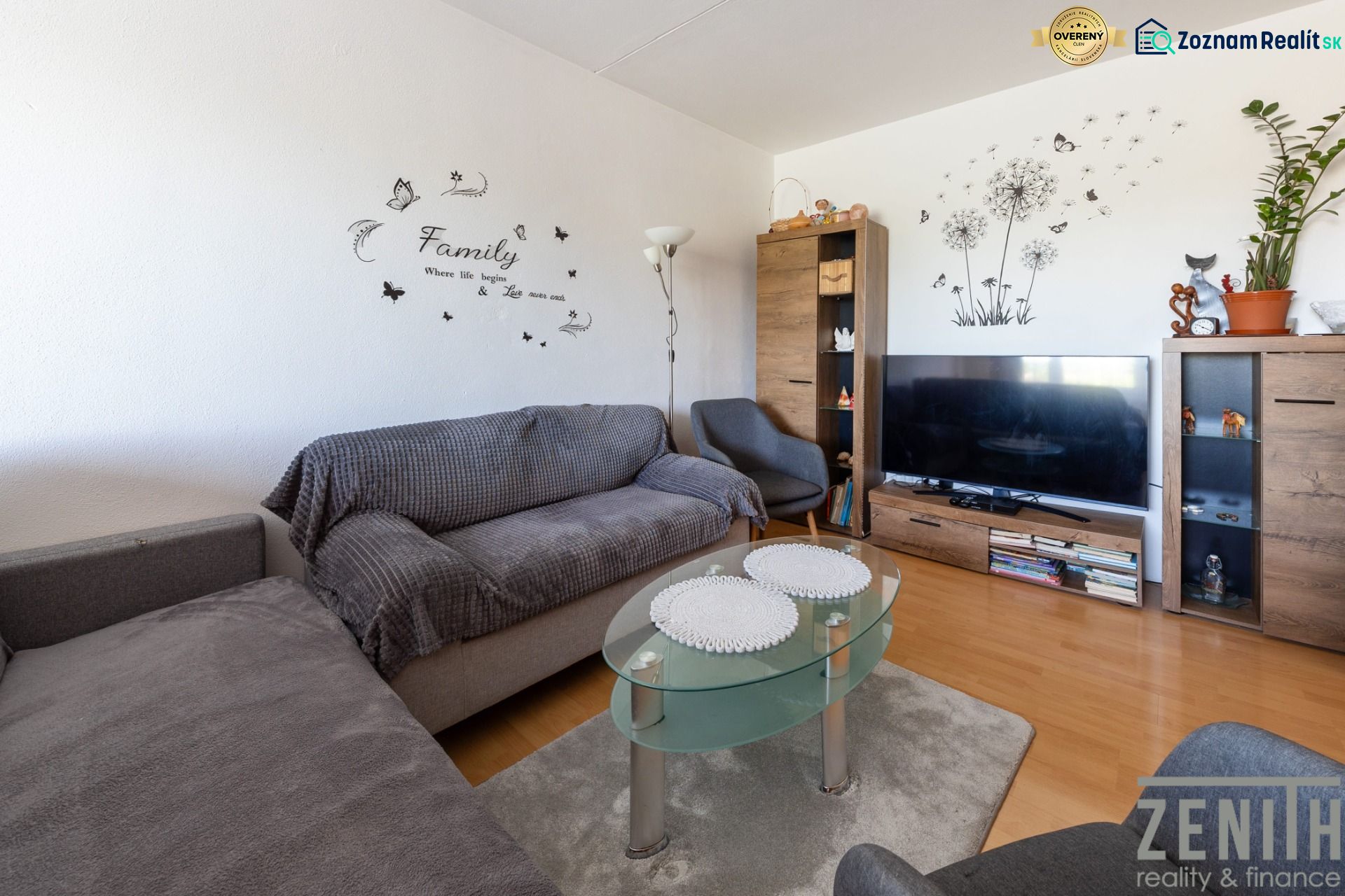 Living room with wood-patterned flooring, a sofa, a glass table, and a television.