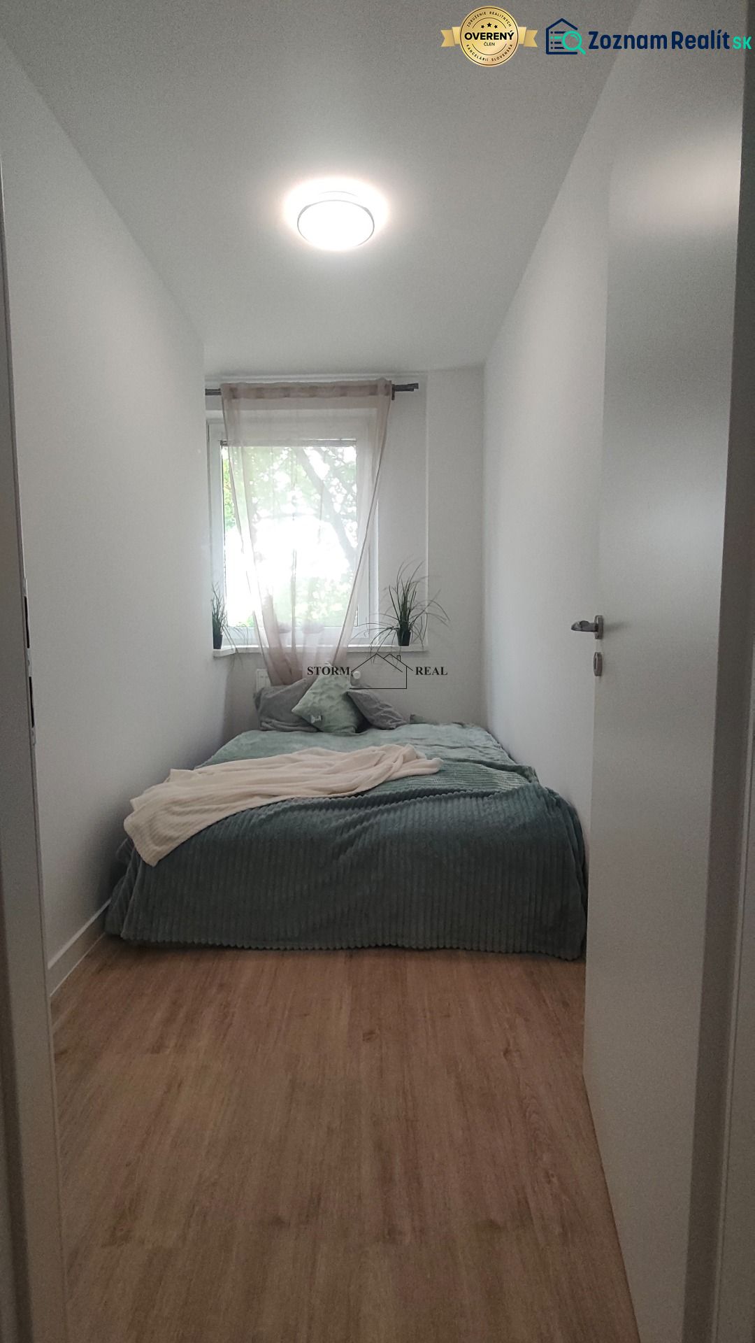 A bedroom with a bed, white walls, and a floor with a wood decor in a 4-room apartment.