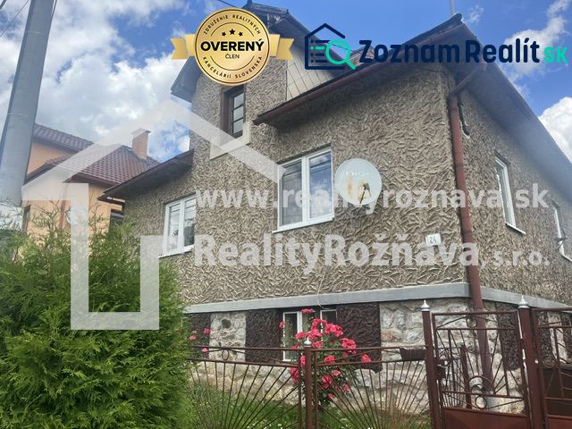 A family house in Rudná with a textured facade, a green fence, and flowers in the garden.