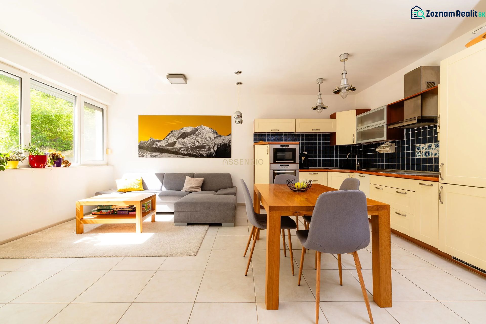 Living room with kitchen, light sofa, dining table, large windows, art on the wall.