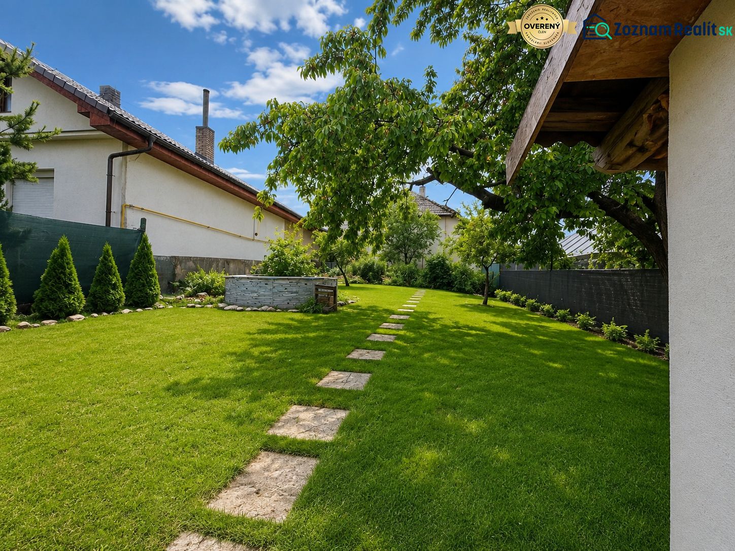 The garden of a family house in Šalgovce with a lawn, trees, and a paved walkway.