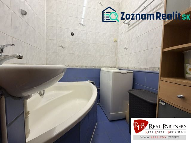A bathroom in a studio apartment with a bathtub and a washing machine, tiled with white and blue tiles.