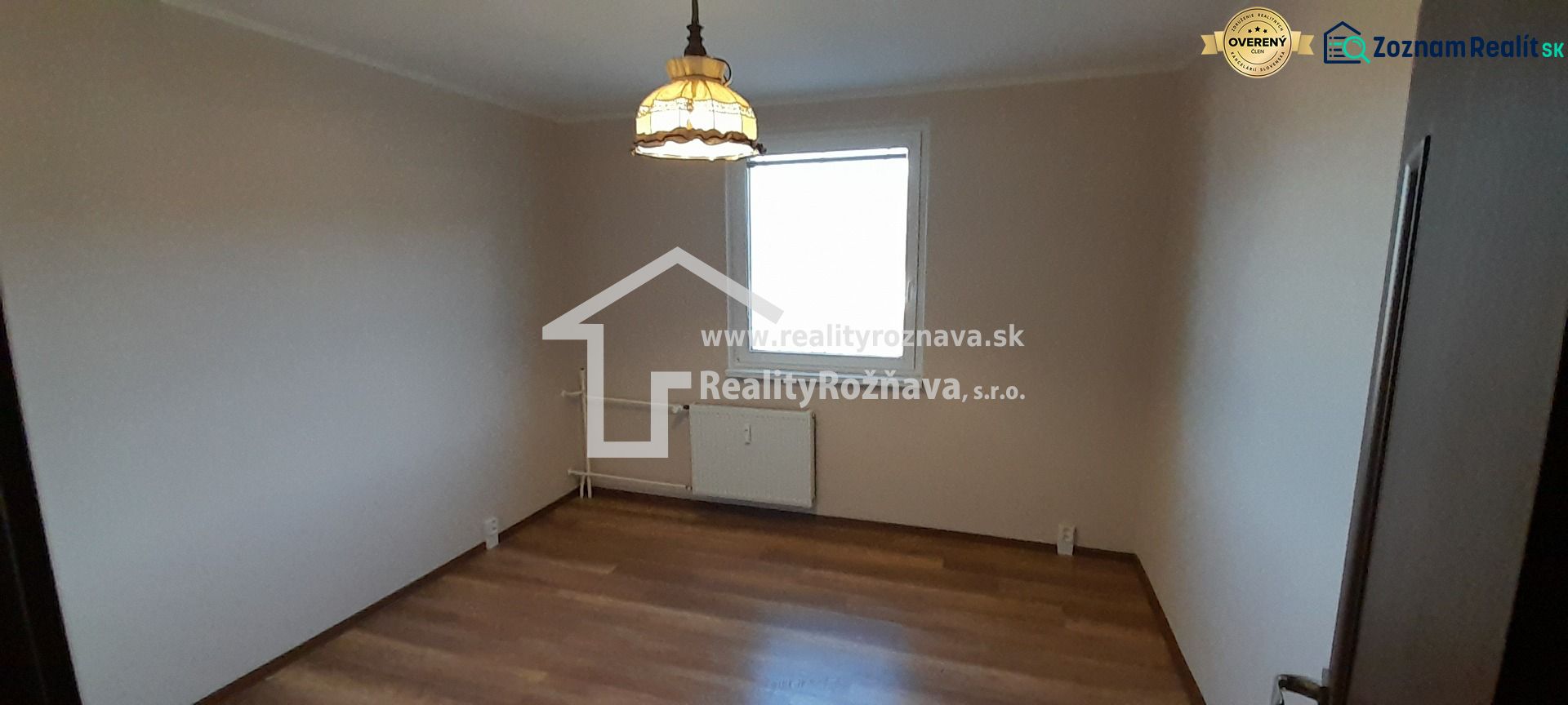 A room in a 2-room apartment with a wood-decor floor and a light above the radiator.