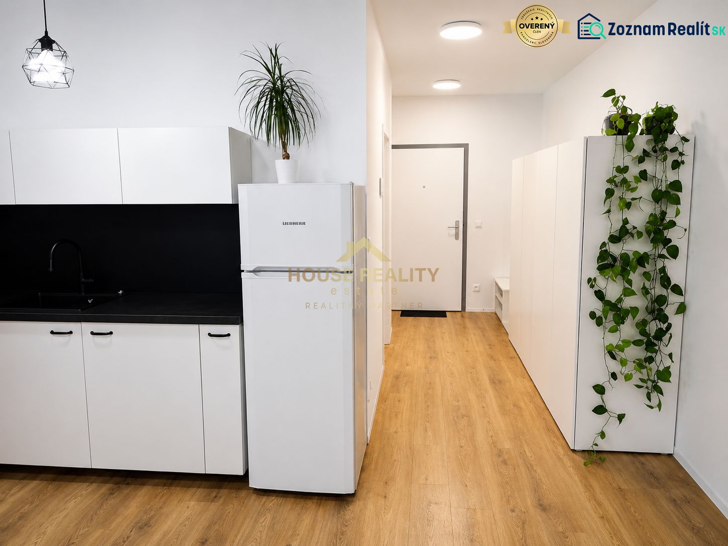 A kitchen in a studio apartment with a black sink, white cabinets, and a wood-patterned floor.