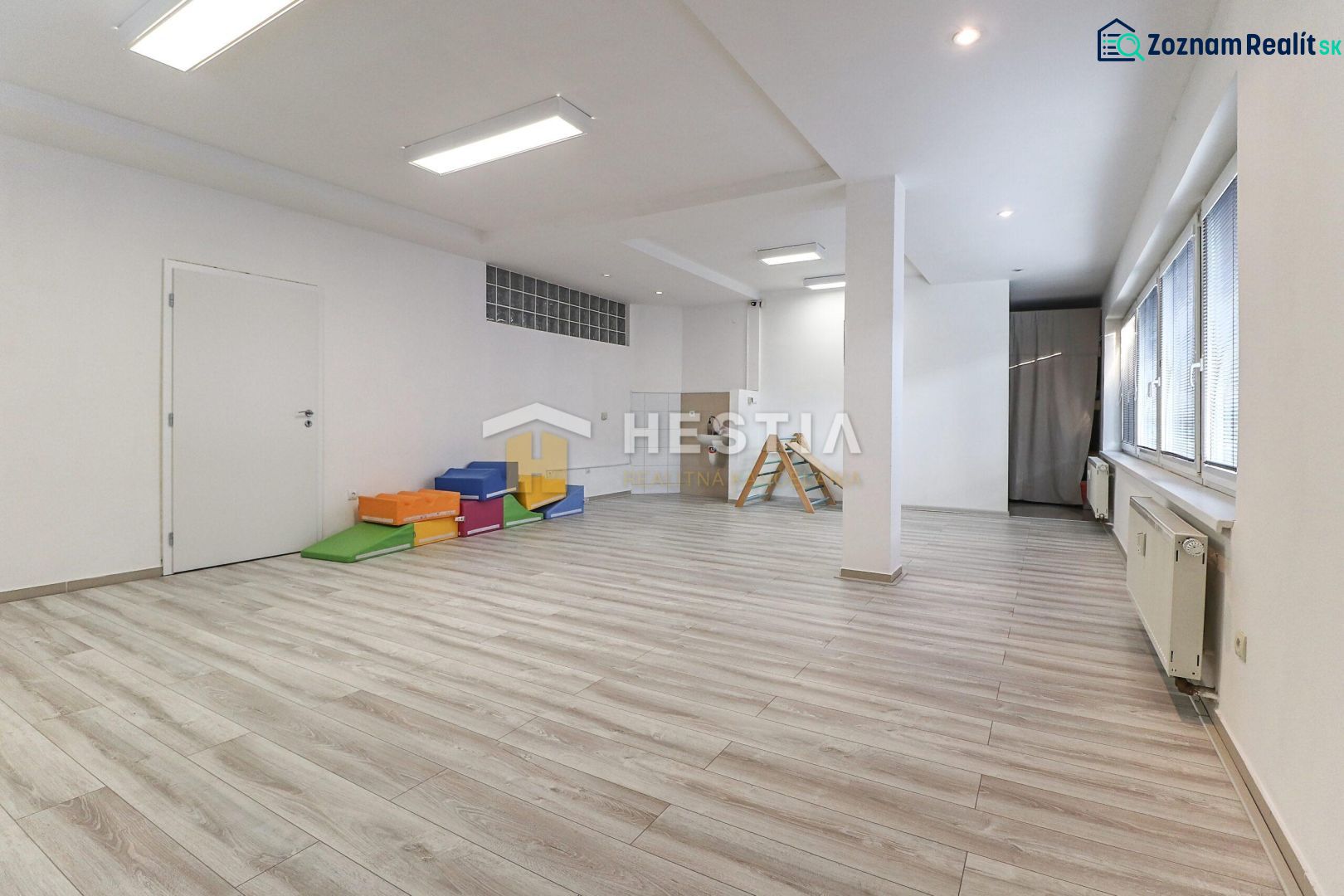 Commercial spaces with wood-patterned flooring, ceiling lighting, colorful mattresses, and windows.