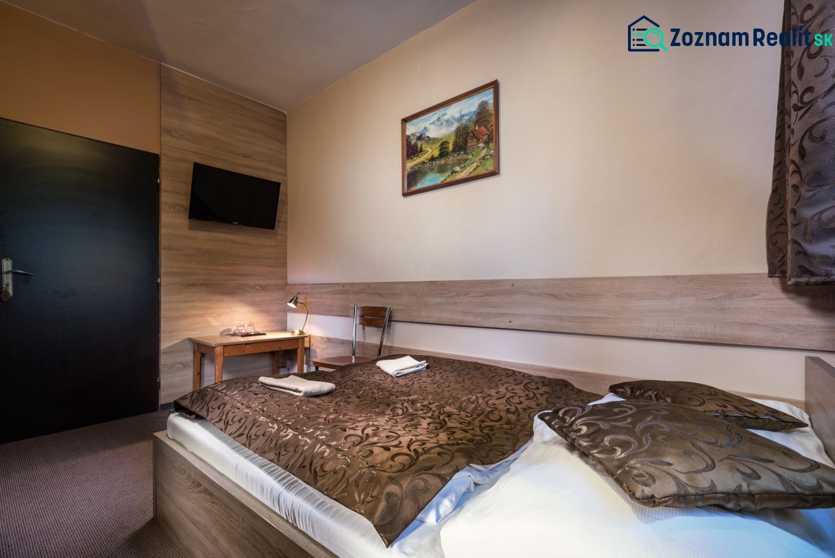 A hotel room interior with a bed, decorative blanket, and a TV on the wall.