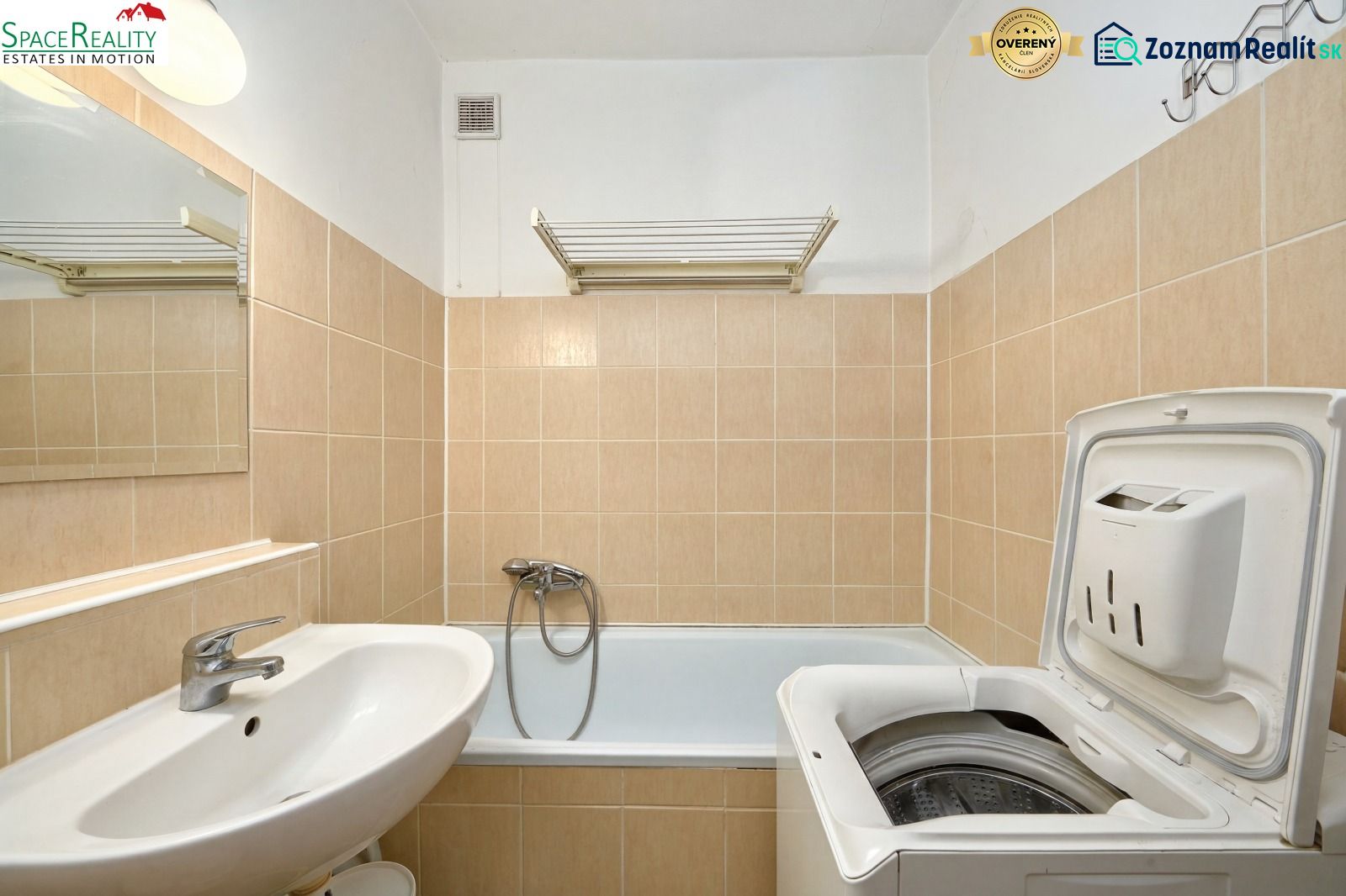 A bathroom with a washing machine and a bathtub in a 2-room apartment with beige tiles.