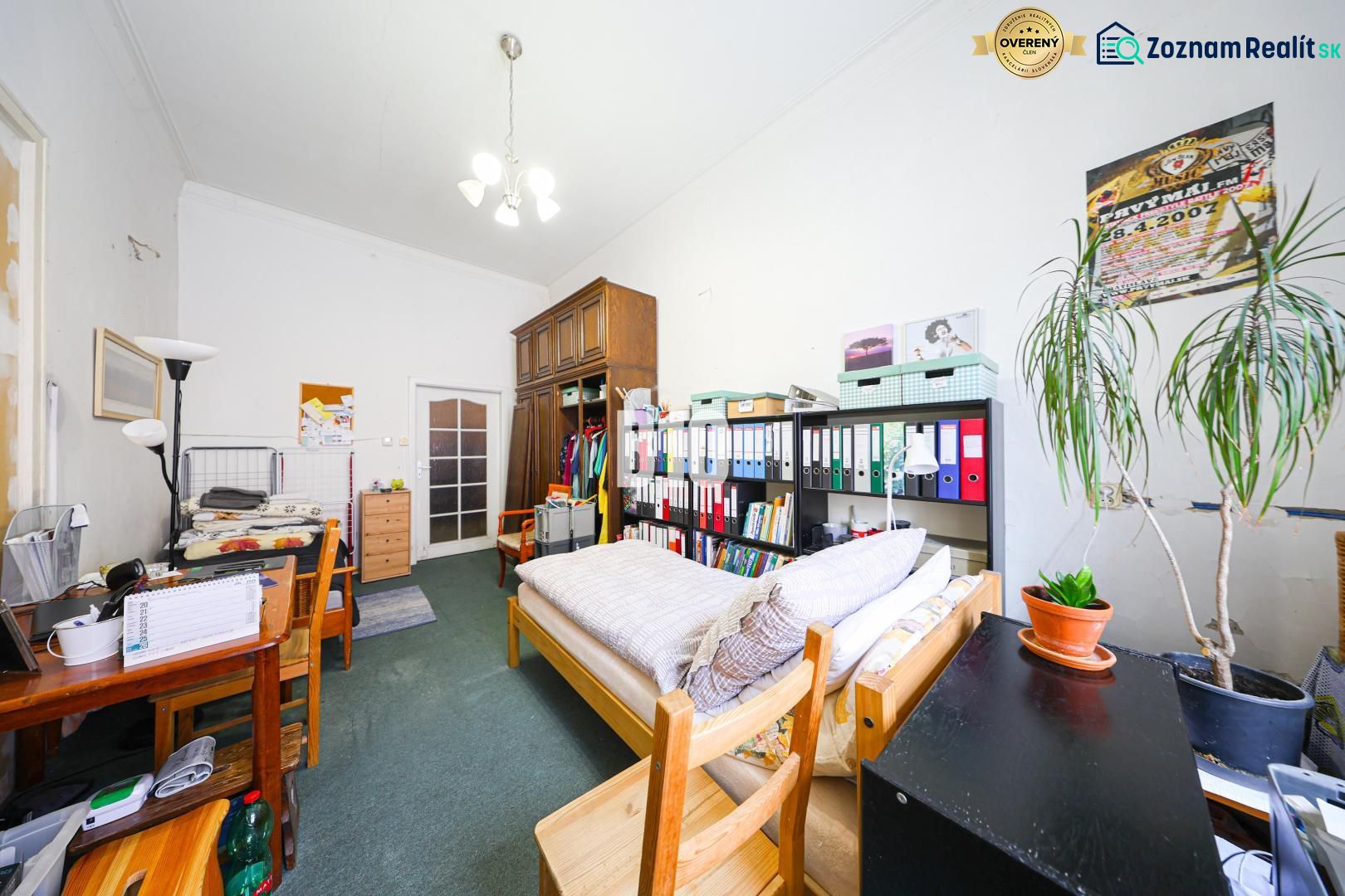Room with a bed, shelves with documents, a desk, and a plant in a two-room apartment.