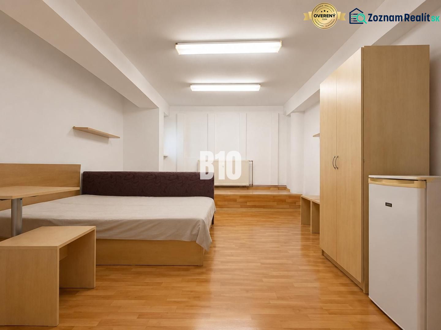 A bedroom in a two-room apartment with a wooden decor floor and simple furniture.